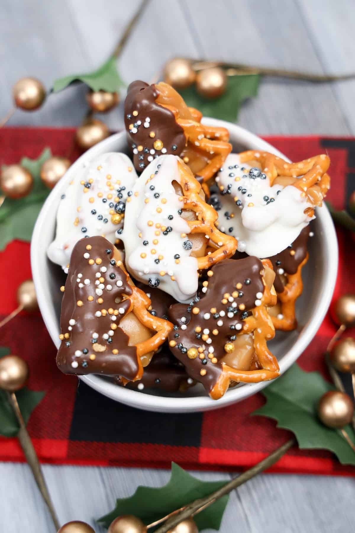 Holiday caramel pretzel bites coated in white and dark chocolate and decorated with sprinkles in a white bowl.