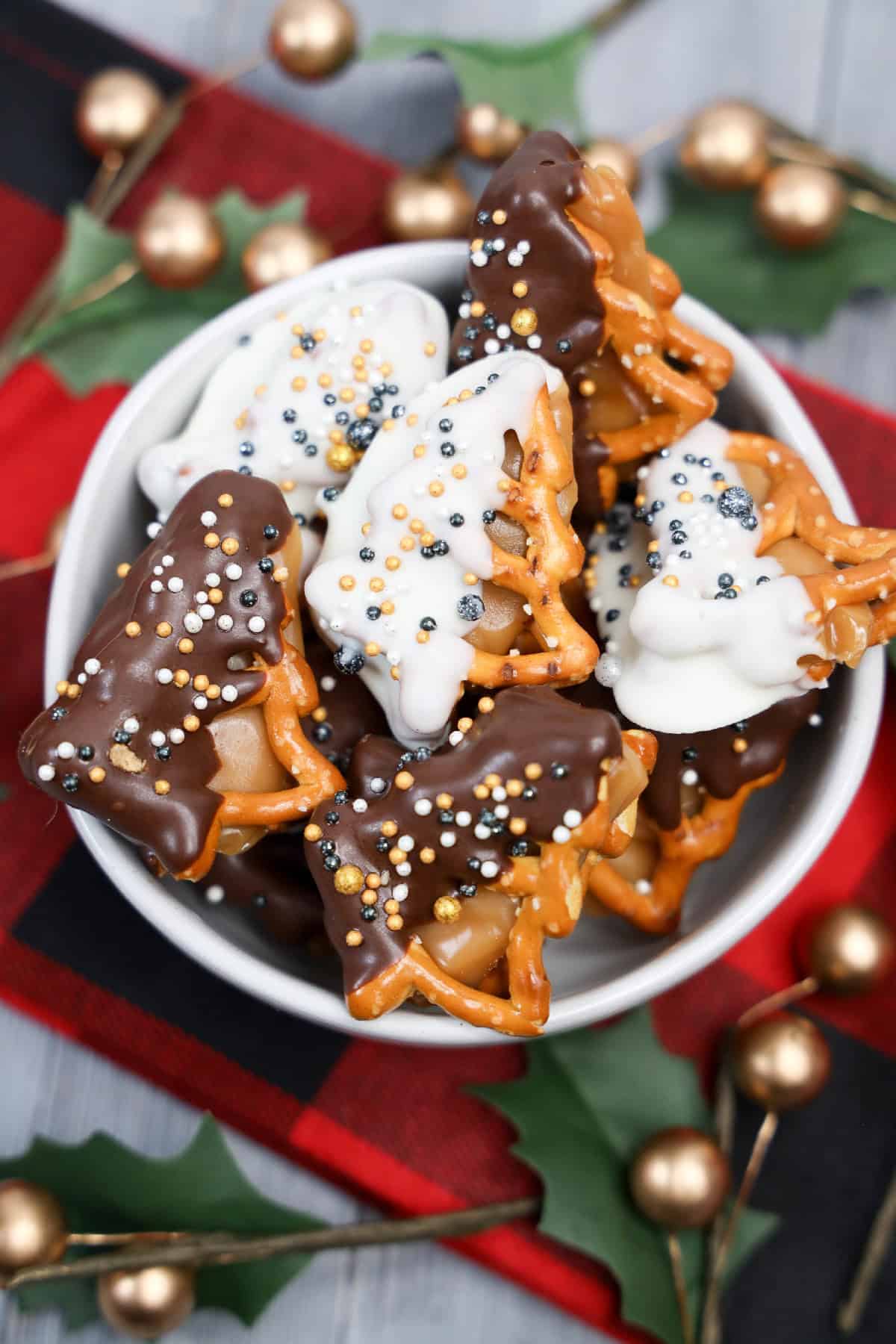 Chocolate-covered caramel pretzel bites with holiday sprinkles served in a small white bowl.