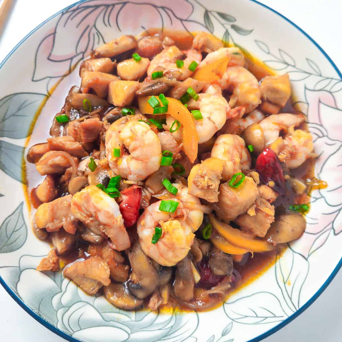 Shrimp and chicken stir fry with mushrooms, bell peppers, and green onions served in a floral bowl.