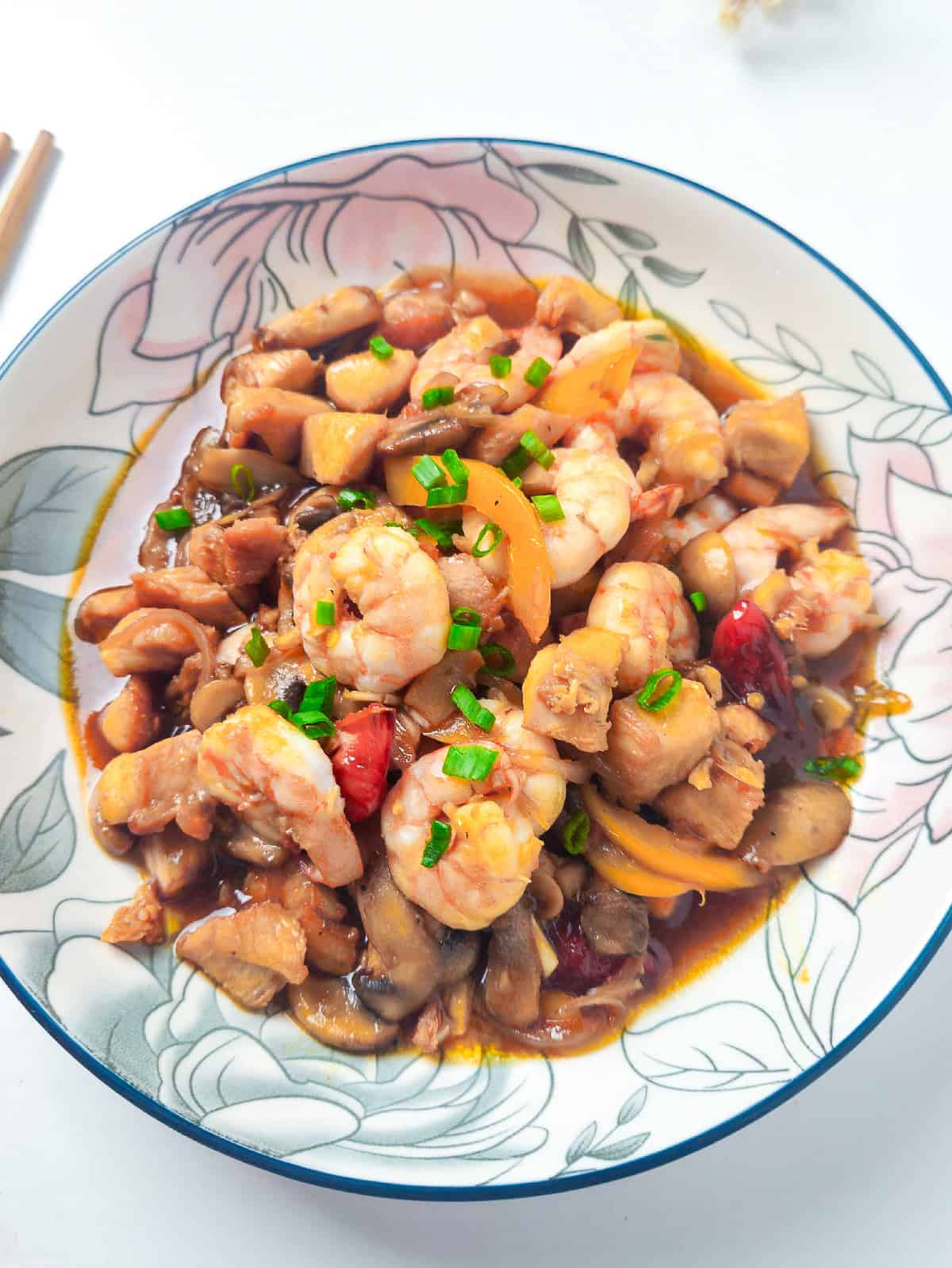 Shrimp and chicken stir fry with mushrooms and peppers served in a floral bowl.