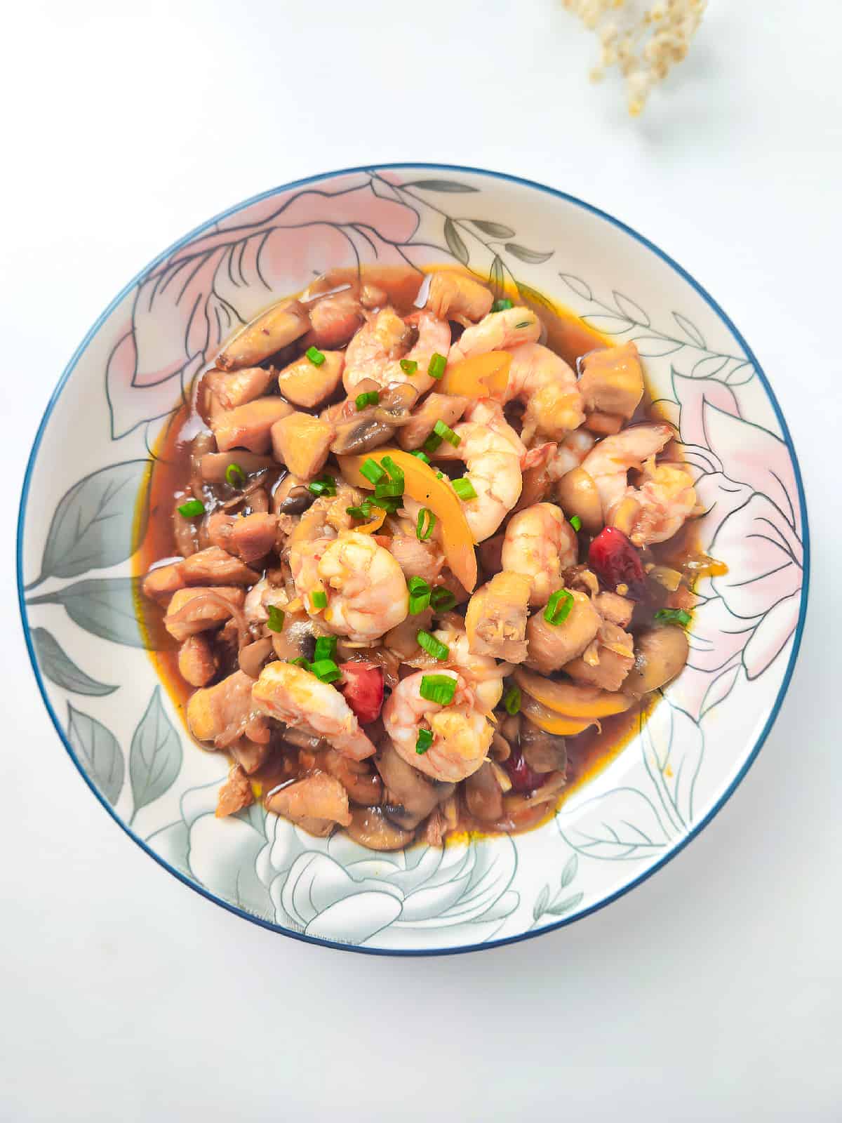 Top view of shrimp and chicken stir fry with mushrooms and peppers in a decorative bowl.