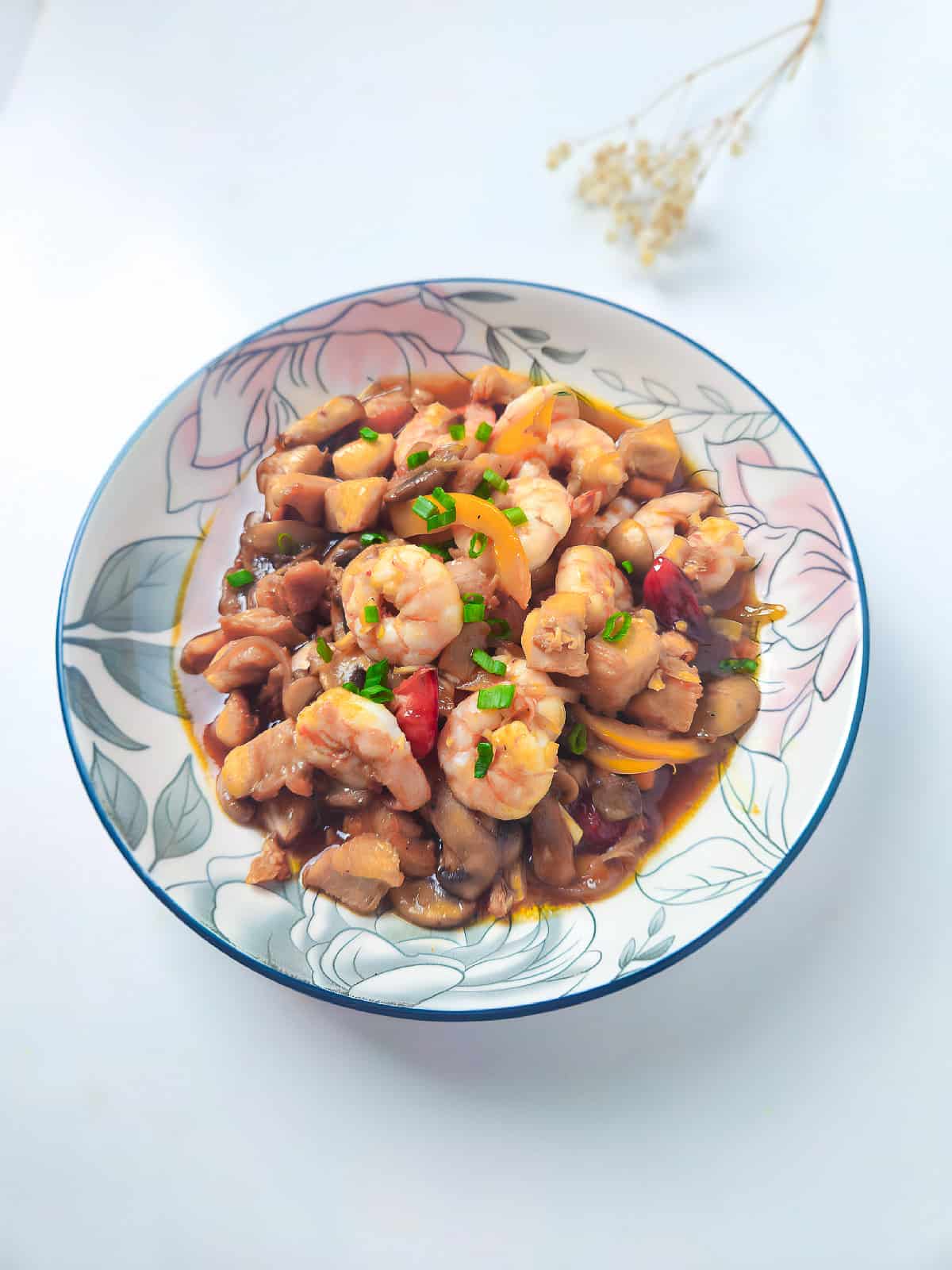 Shrimp and chicken stir fry plated in a floral bowl on a bright white background with garnish decor.