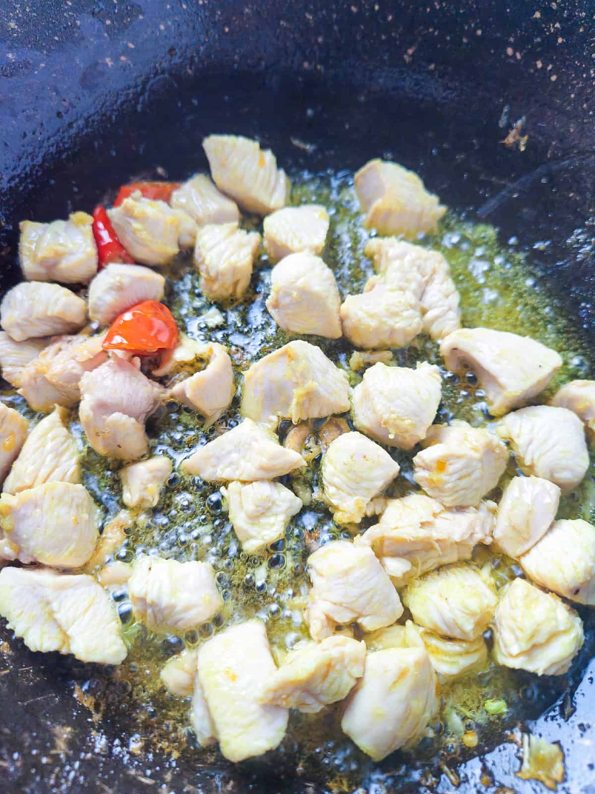 Diced chicken cooking in oil with garlic and red chili peppers in a wok.
