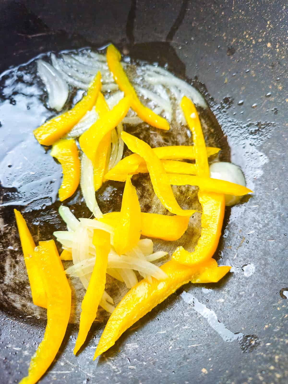 Sliced yellow bell pepper and onions sautéing in oil inside a wok.