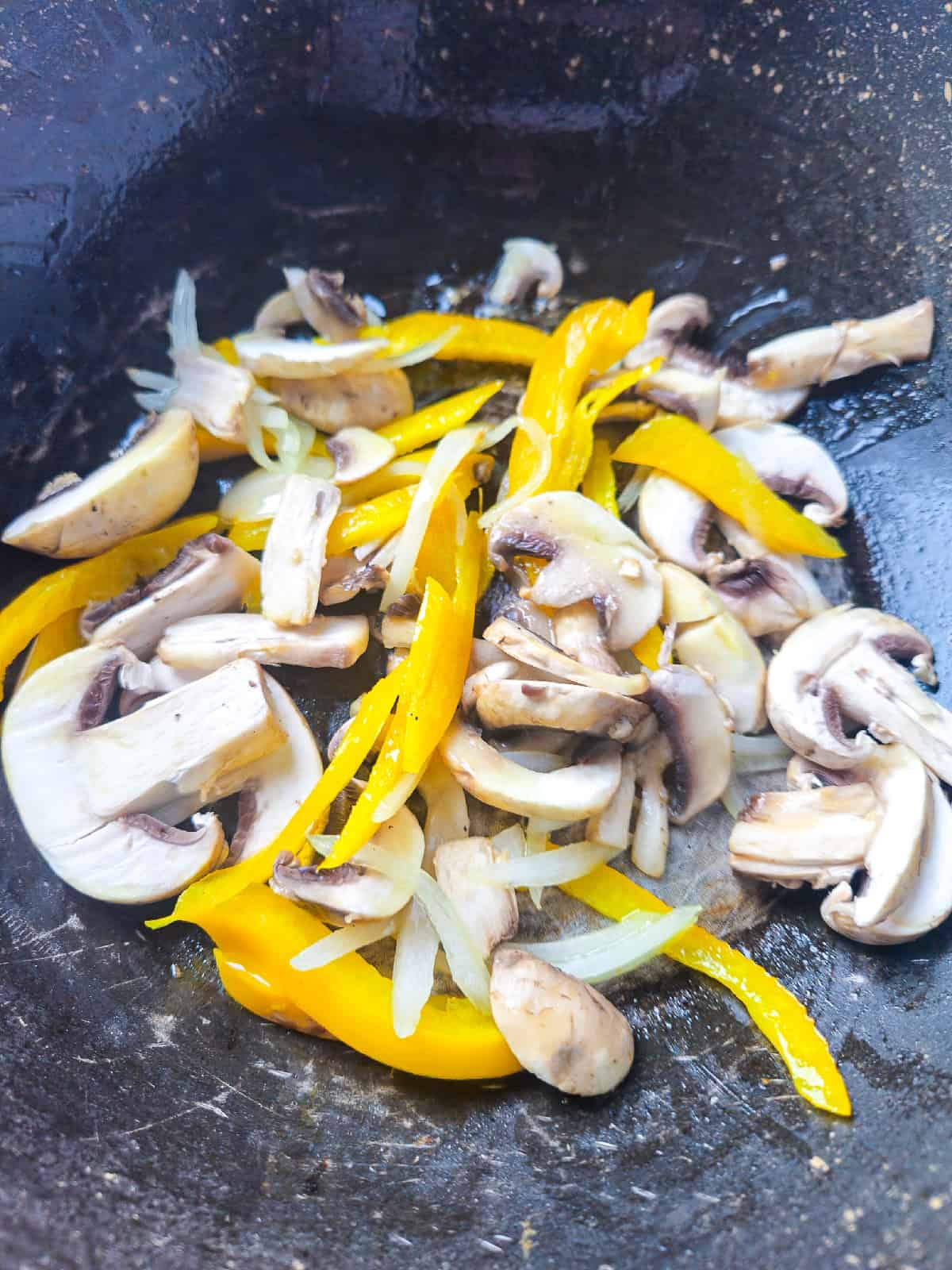 Mushrooms, onions, and bell pepper strips cooking together in a wok.