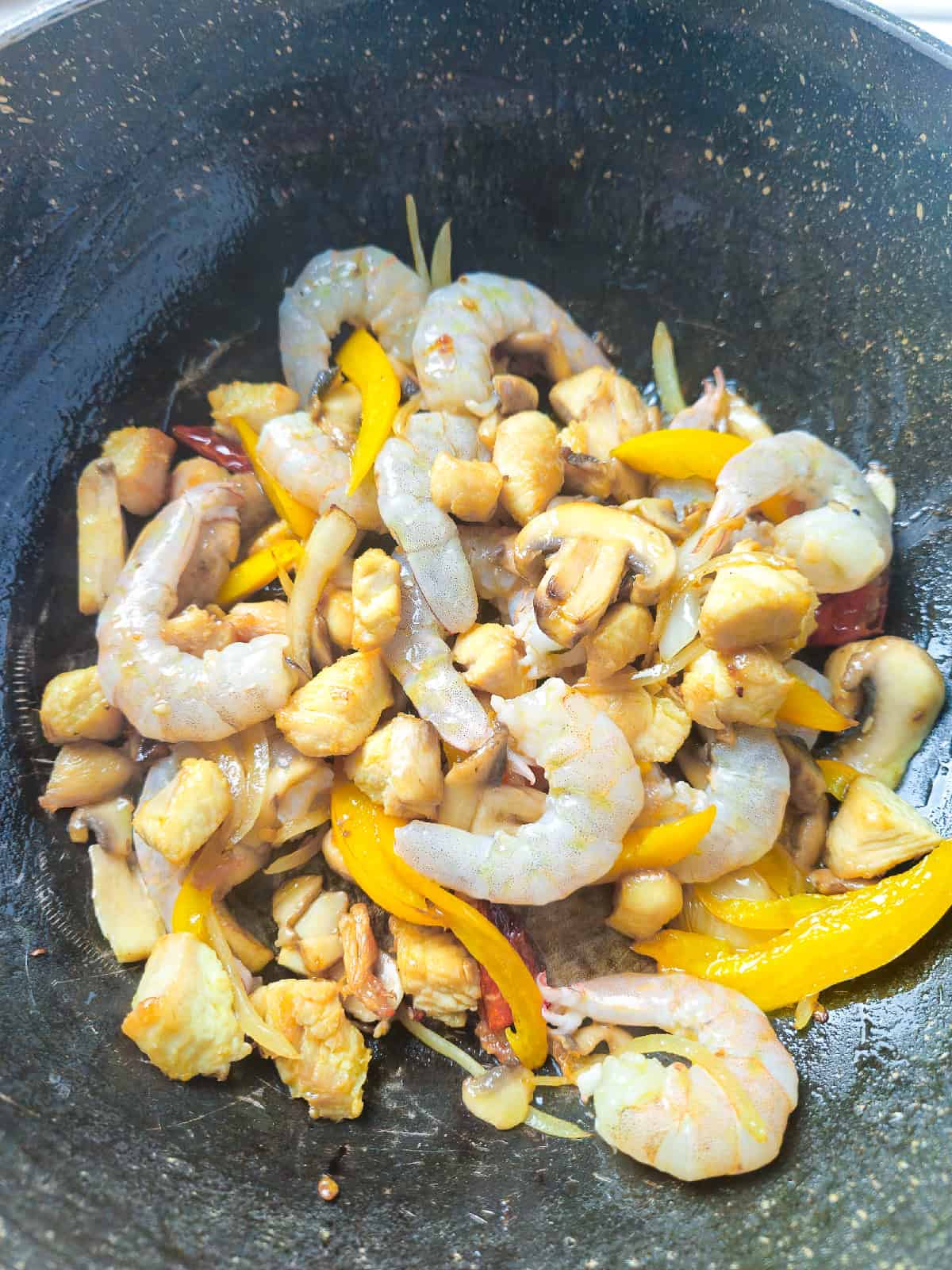 Raw shrimp added into the wok with chicken, mushrooms, and bell pepper.
