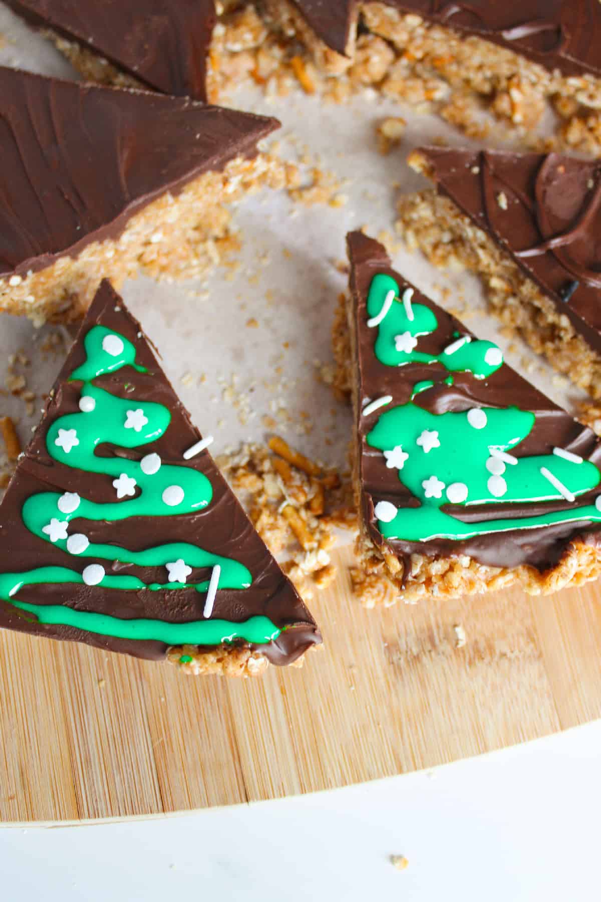 Triangle shaped chocolate peanut butter Christmas tree bars topped with icing and white sprinkles.