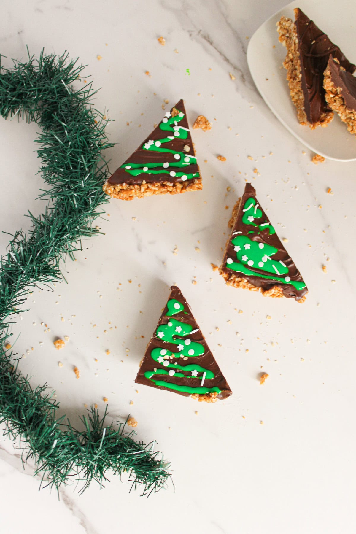 Three chocolate peanut butter Christmas tree treats arranged on a small white plate.