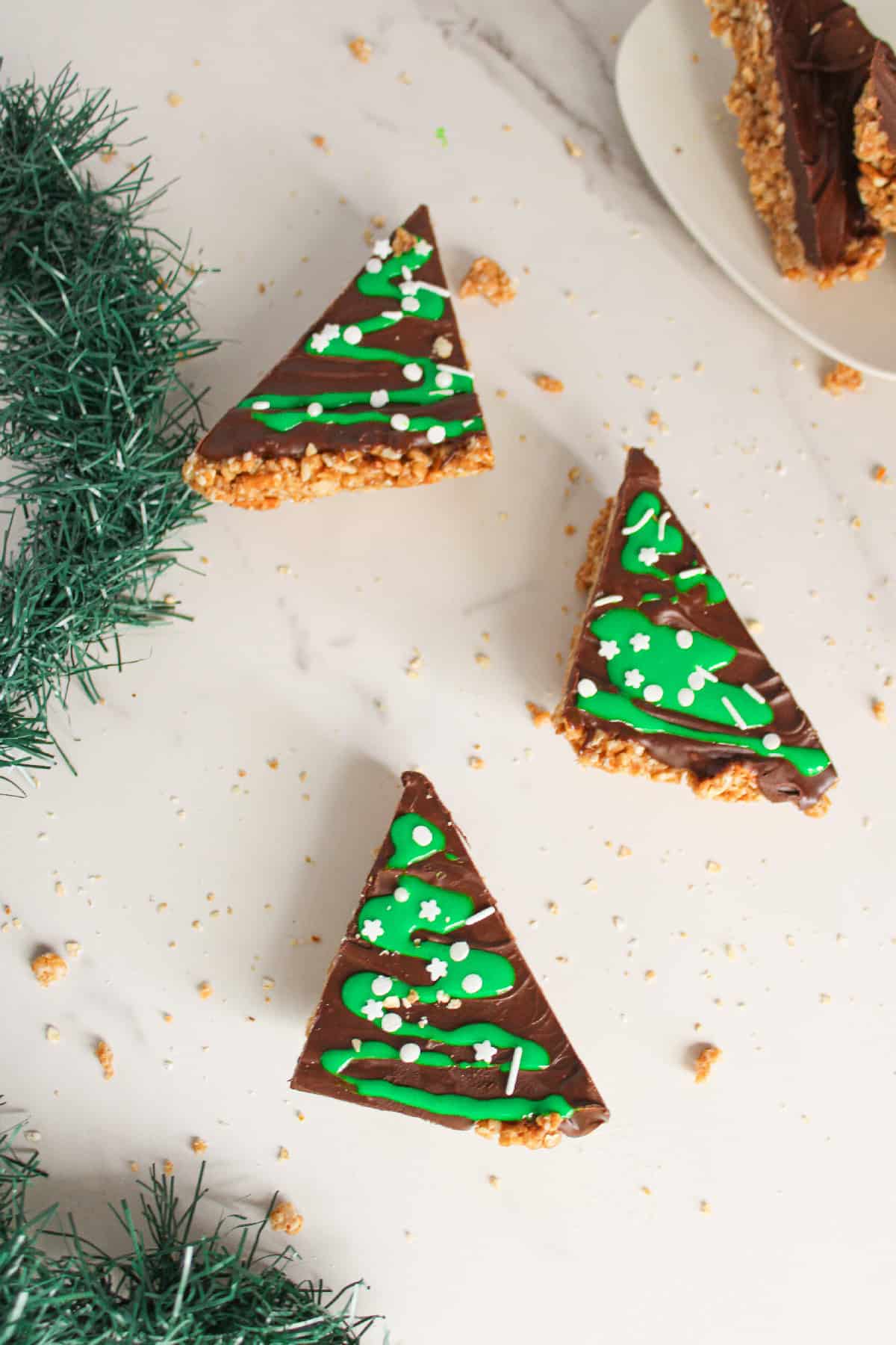 Chocolate peanut butter Christmas tree bars decorated with green icing on a marble surface with holiday garland.