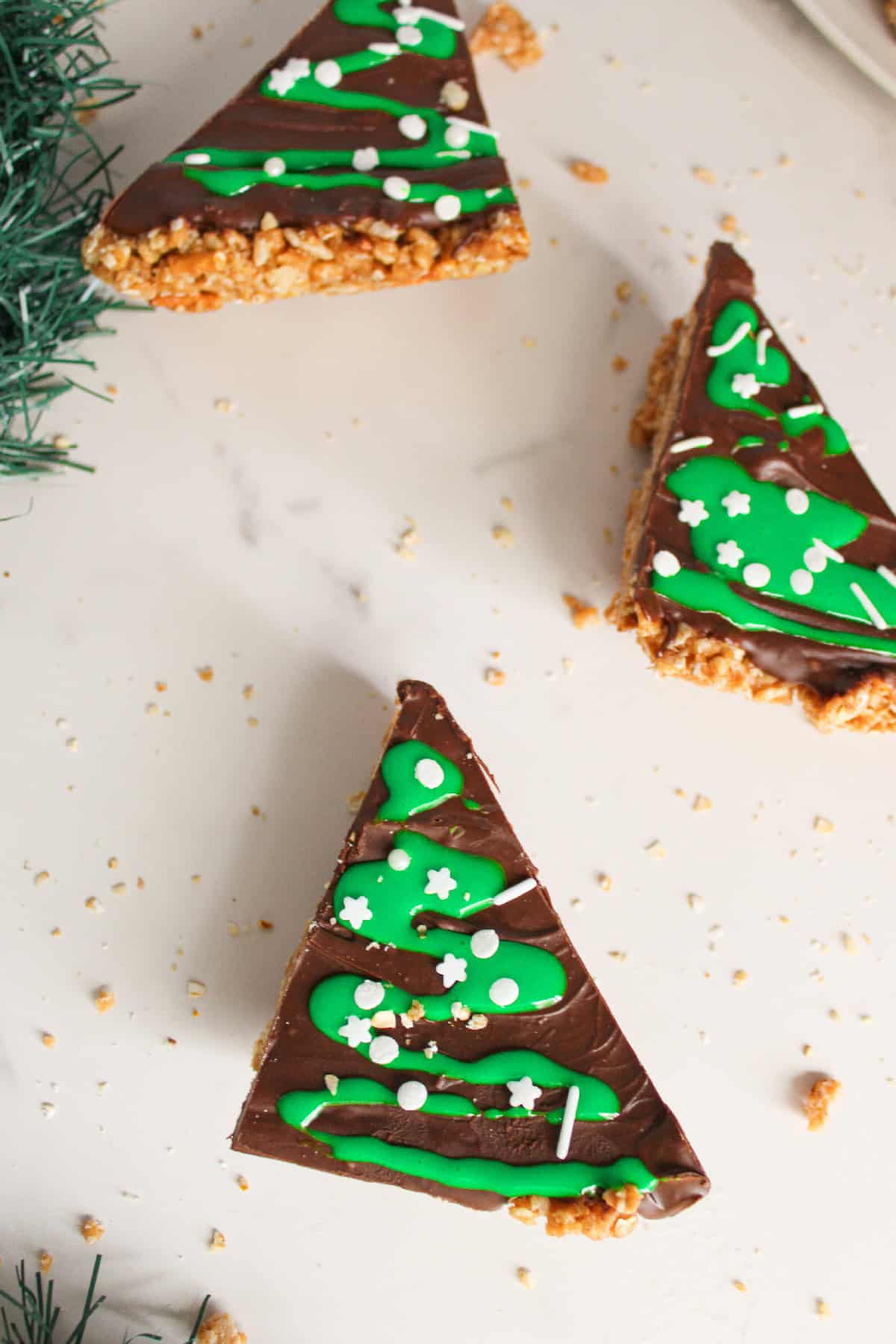 Chocolate peanut butter Christmas tree bars decorated with green icing on a surface with holiday garland.