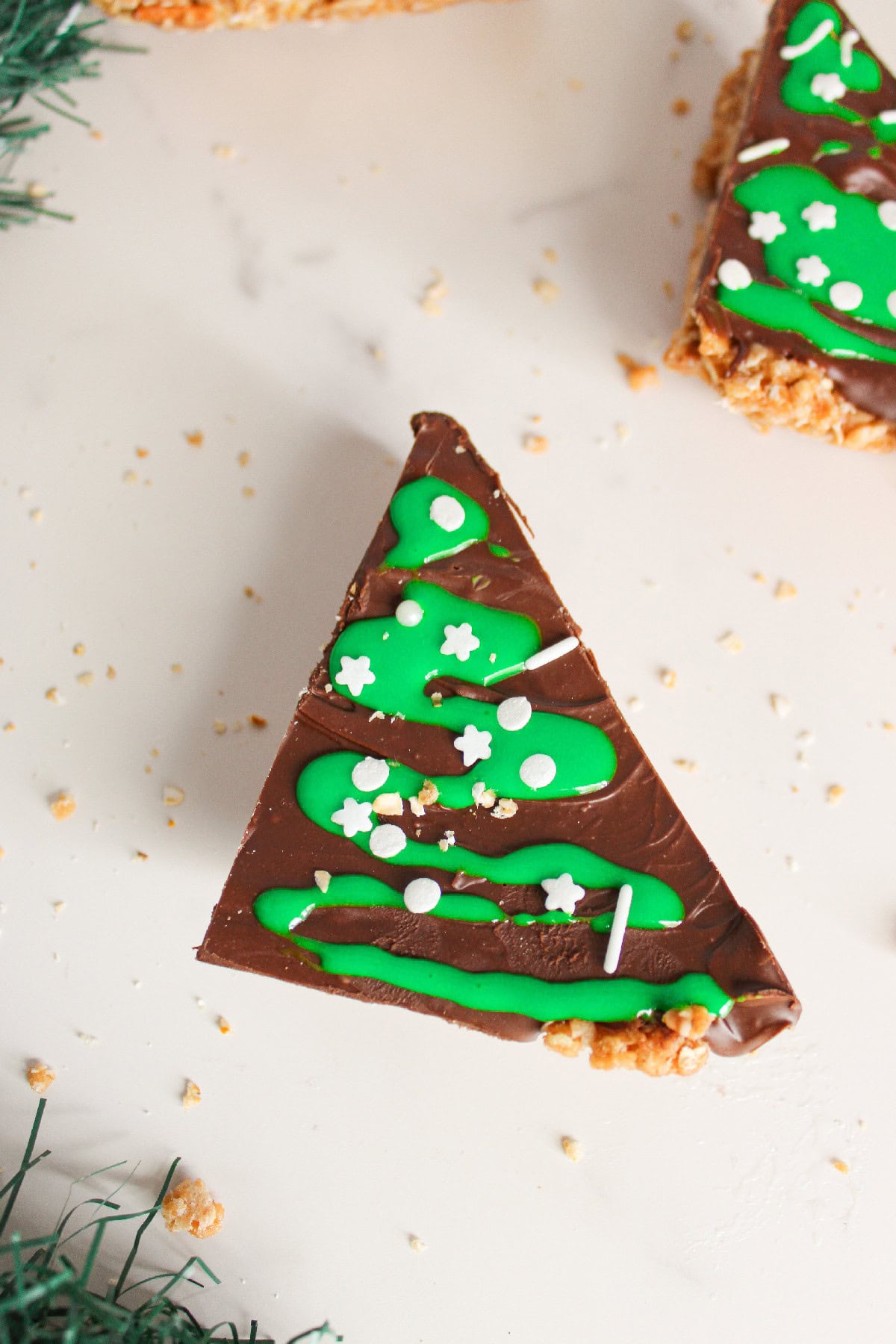 Close up of a chocolate peanut butter Christmas tree bar topped with green icing and sprinkles.