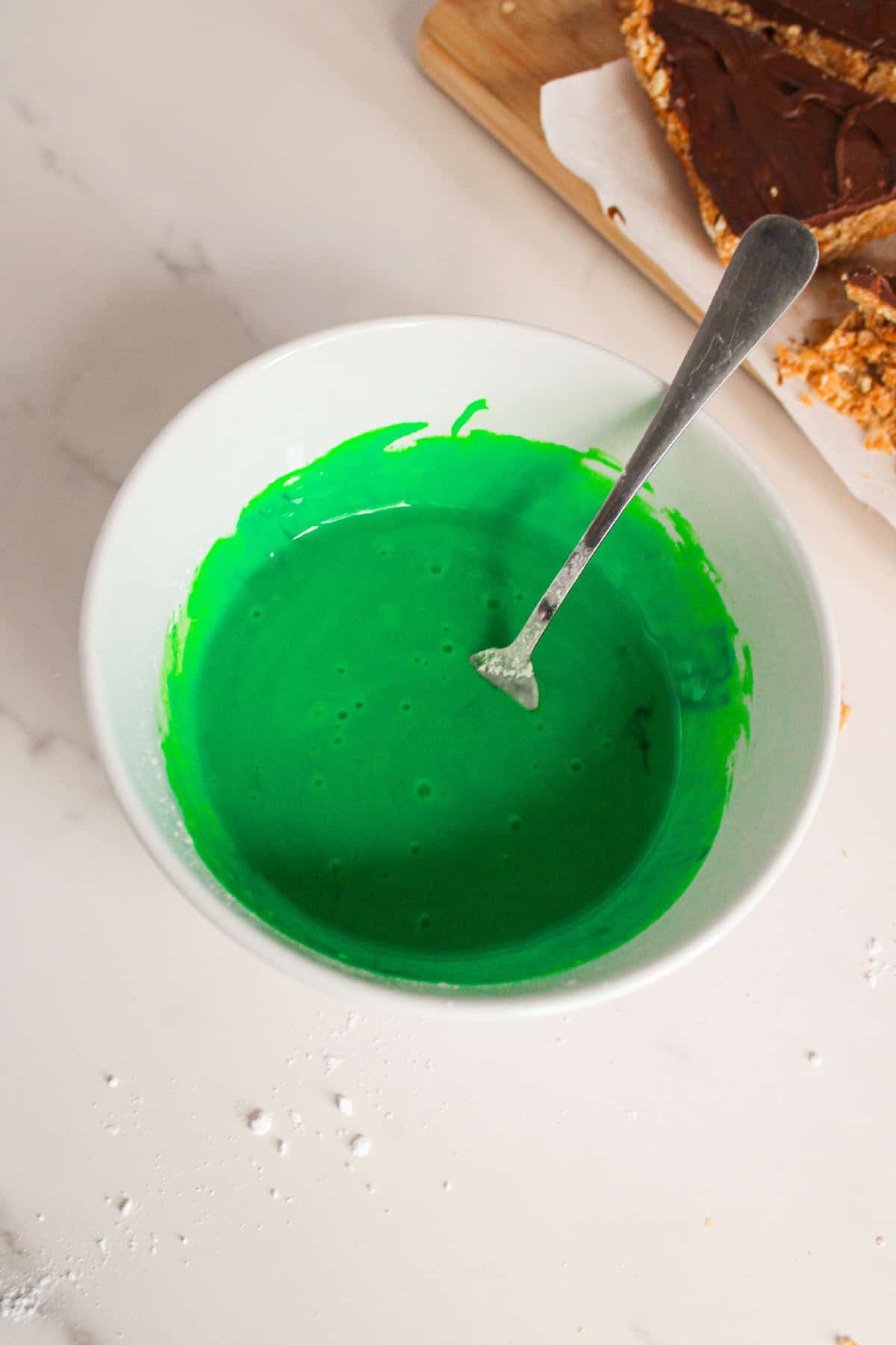 Bright green icing mixture mixed in a bowl for decorating the Christmas tree bars.