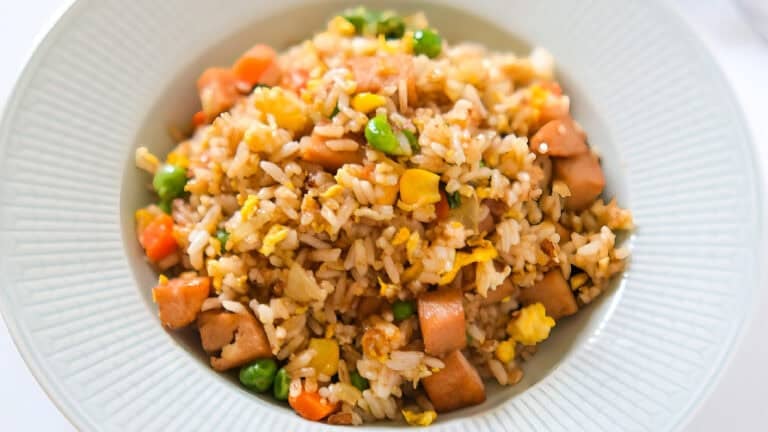 Colorful bowl of spam fried rice mixed with peas, carrots, corn, and scrambled eggs, served in a gray plate.