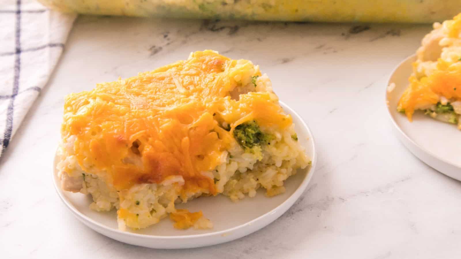Creamy chicken broccoli rice casserole topped with melted cheddar cheese, served on a plate with the casserole dish in the background.