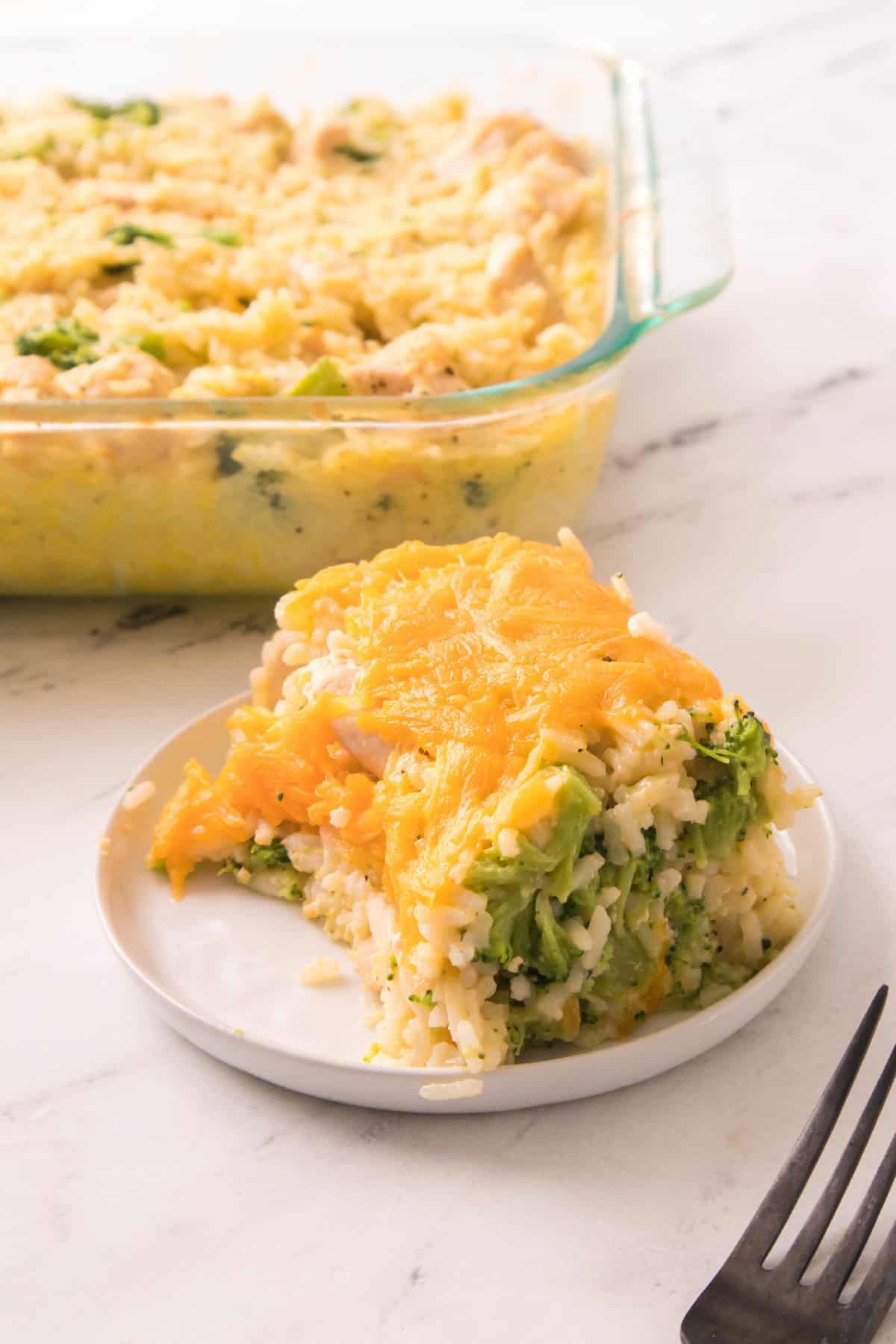 Cheesy chicken broccoli rice casserole slice served on a white plate with melted cheddar on top.