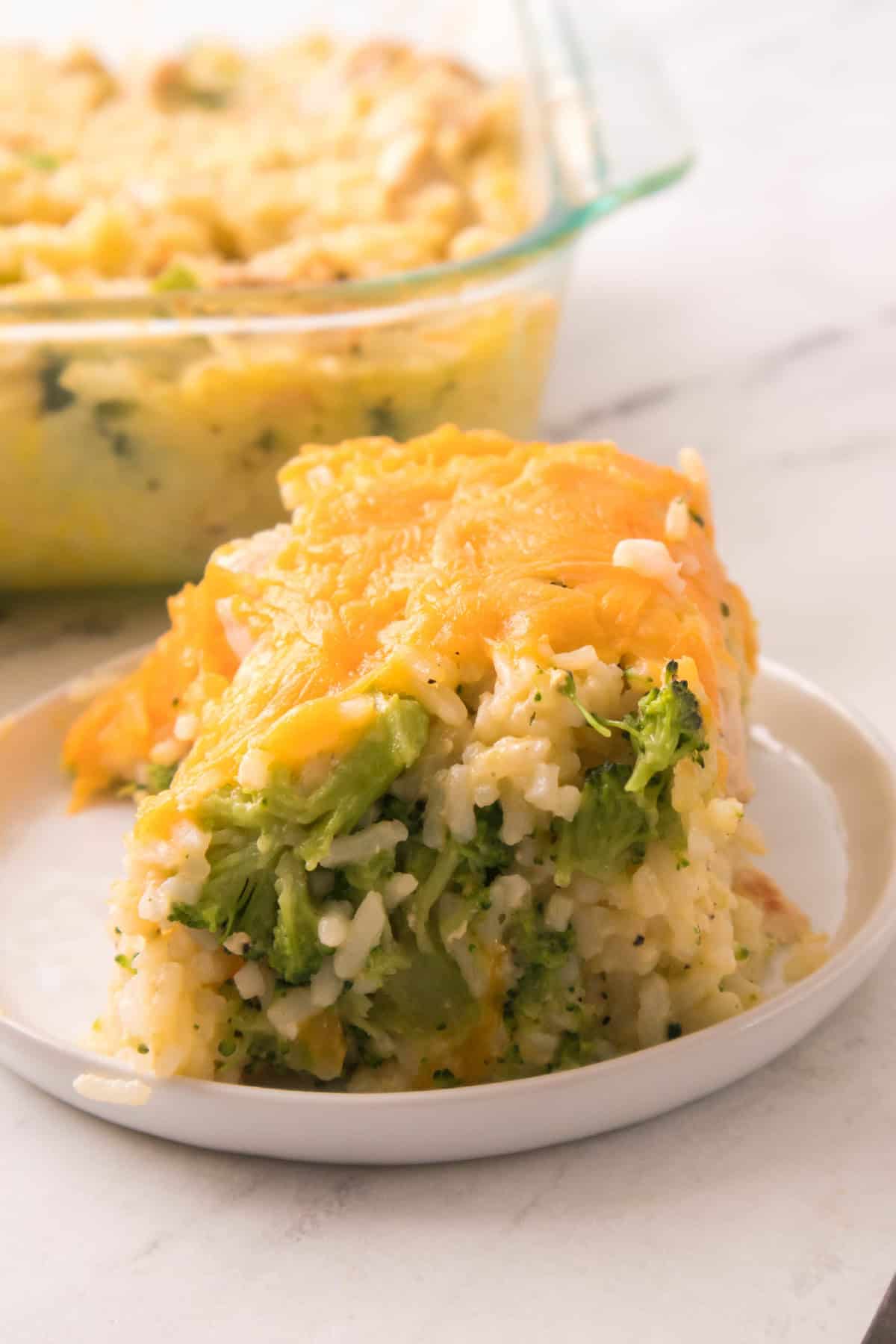 Cheesy chicken broccoli rice casserole slice served on a white plate with melted cheddar on top.