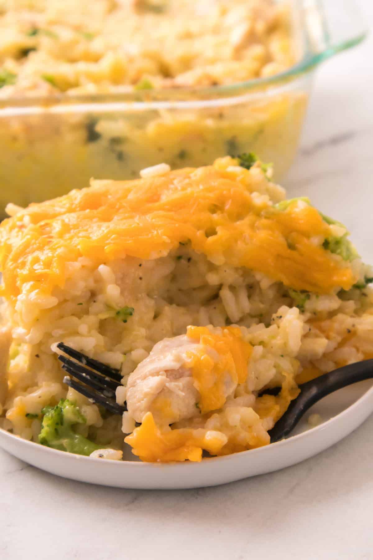 Cheddar-topped chicken broccoli rice casserole on a plate with a fork ready to enjoy.