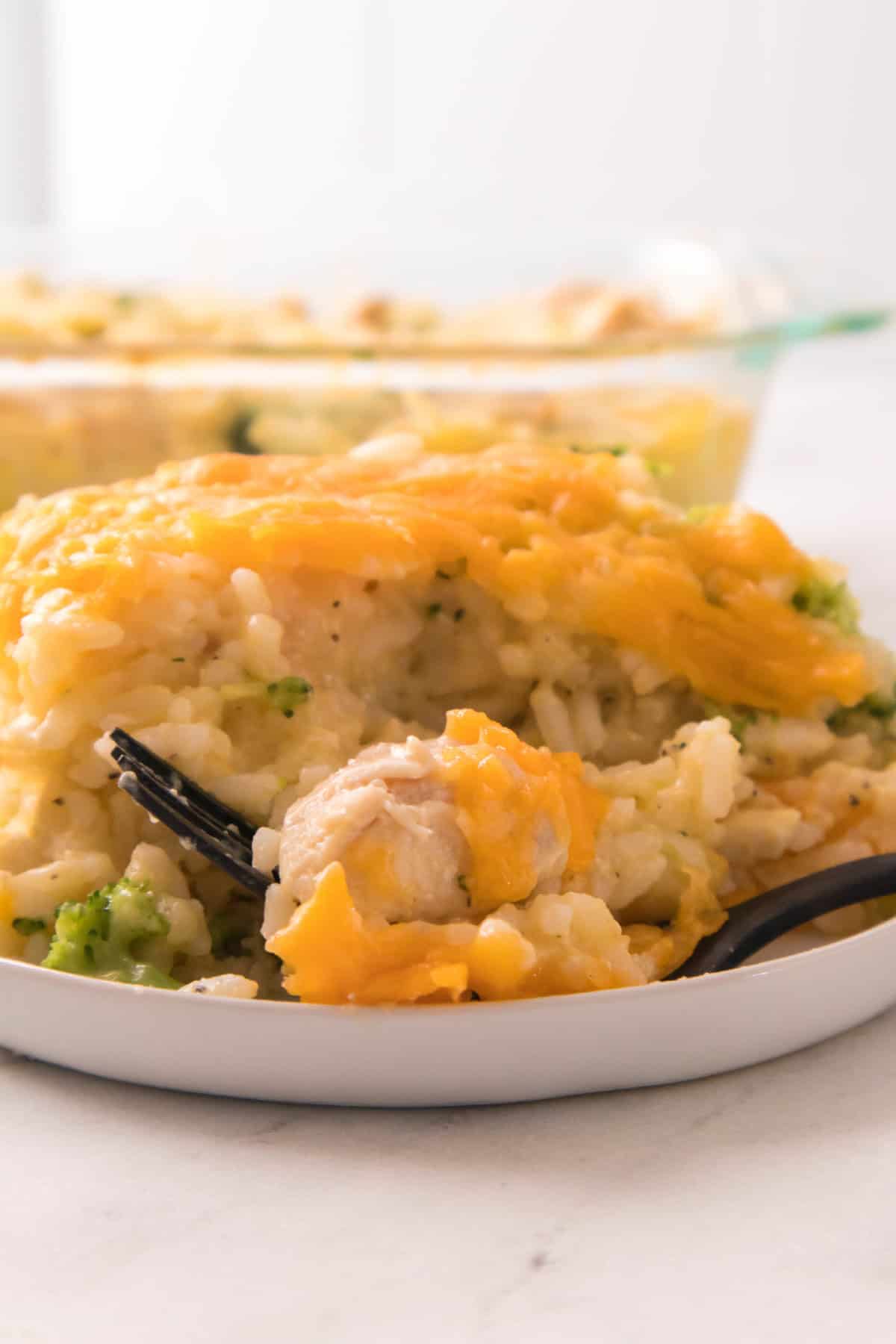 Cheddar-topped chicken broccoli rice casserole on a plate with a fork ready to enjoy.