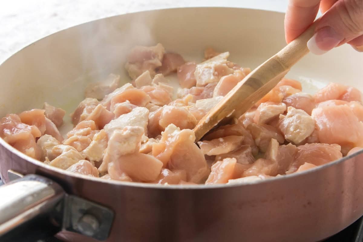 Stirring diced chicken as it cooks in a skillet for easy chicken broccoli rice casserole.