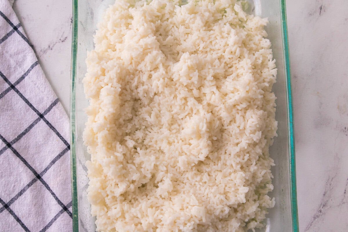 Fluffy cooked white rice spread in a glass casserole dish as the base layer of chicken broccoli rice bake.