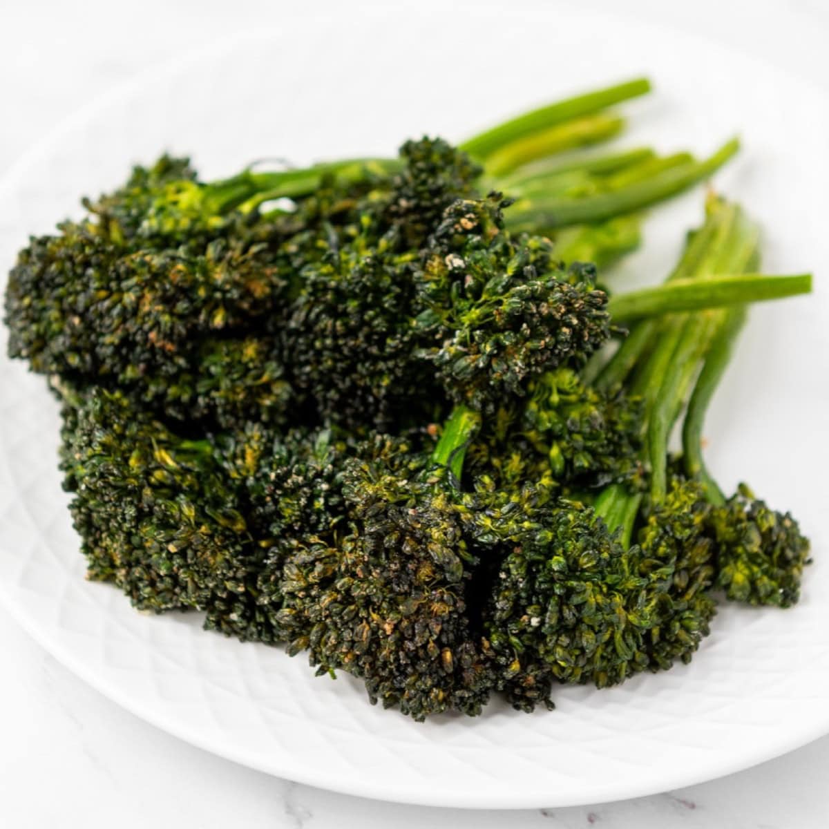 Plate of roasted broccolini with crispy charred tops, served on a white textured plate.