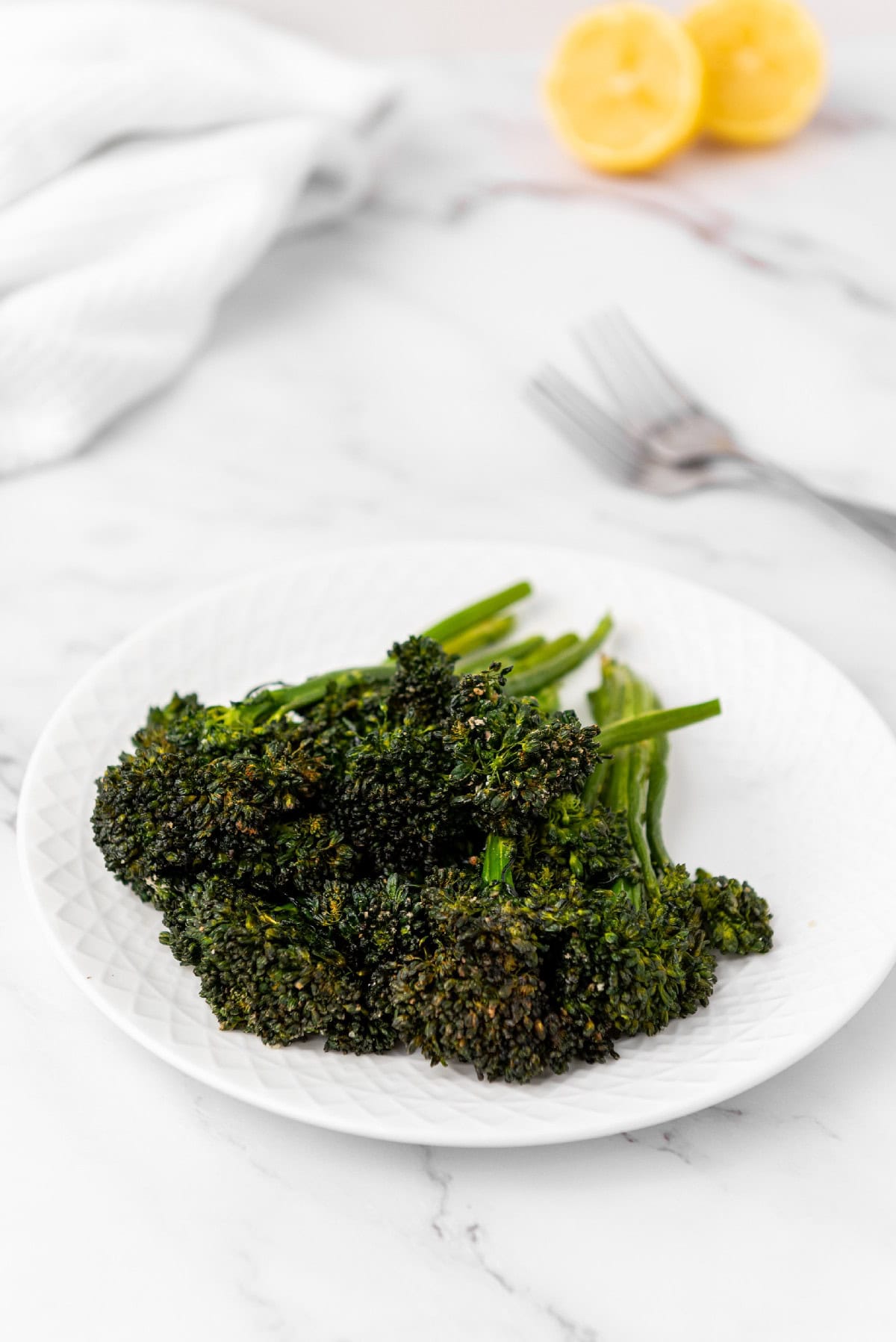 Air fryer broccolini on a plate with lemon and forks in the background.