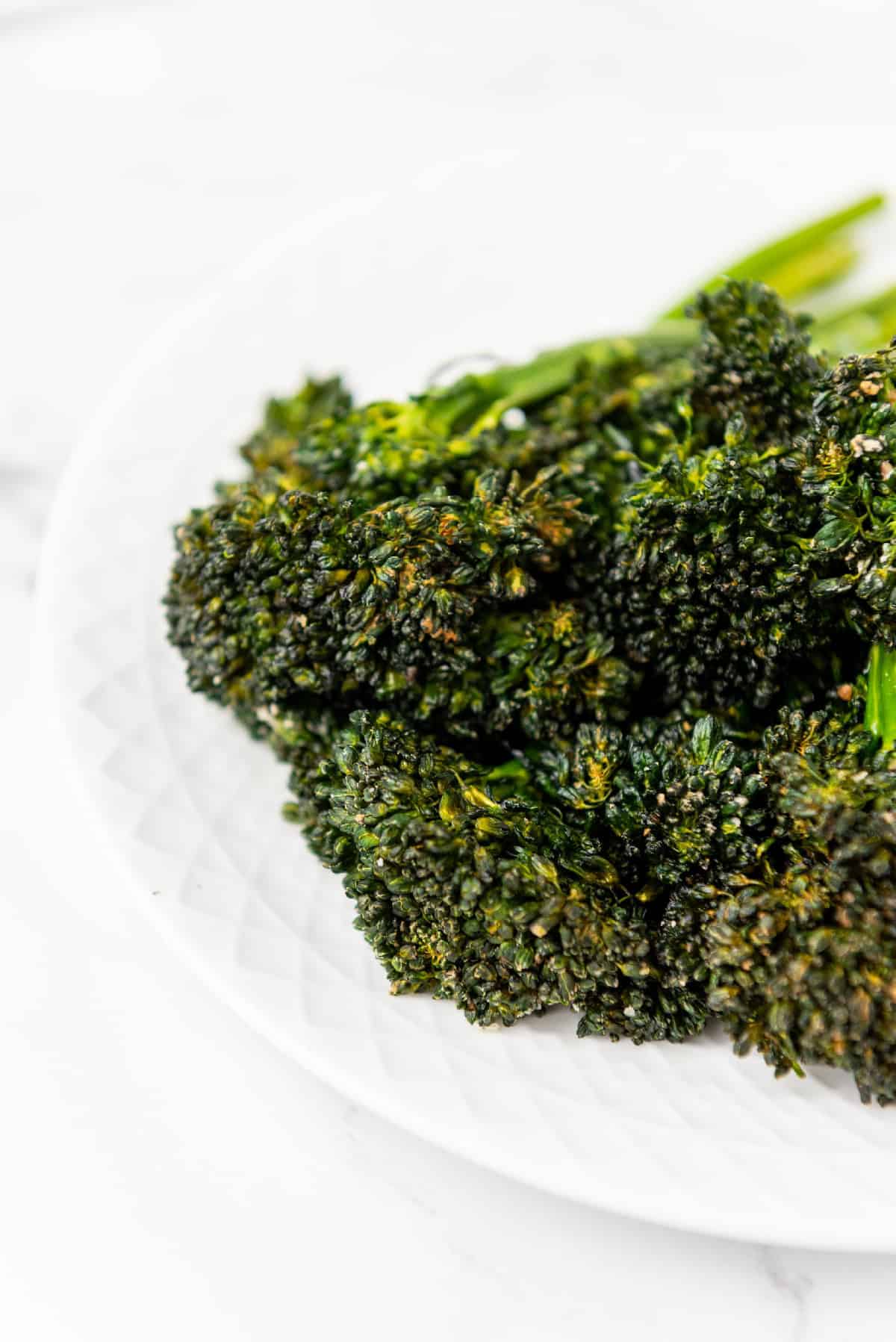 Air fryer broccolini on a plate with lemon and forks in the background.
