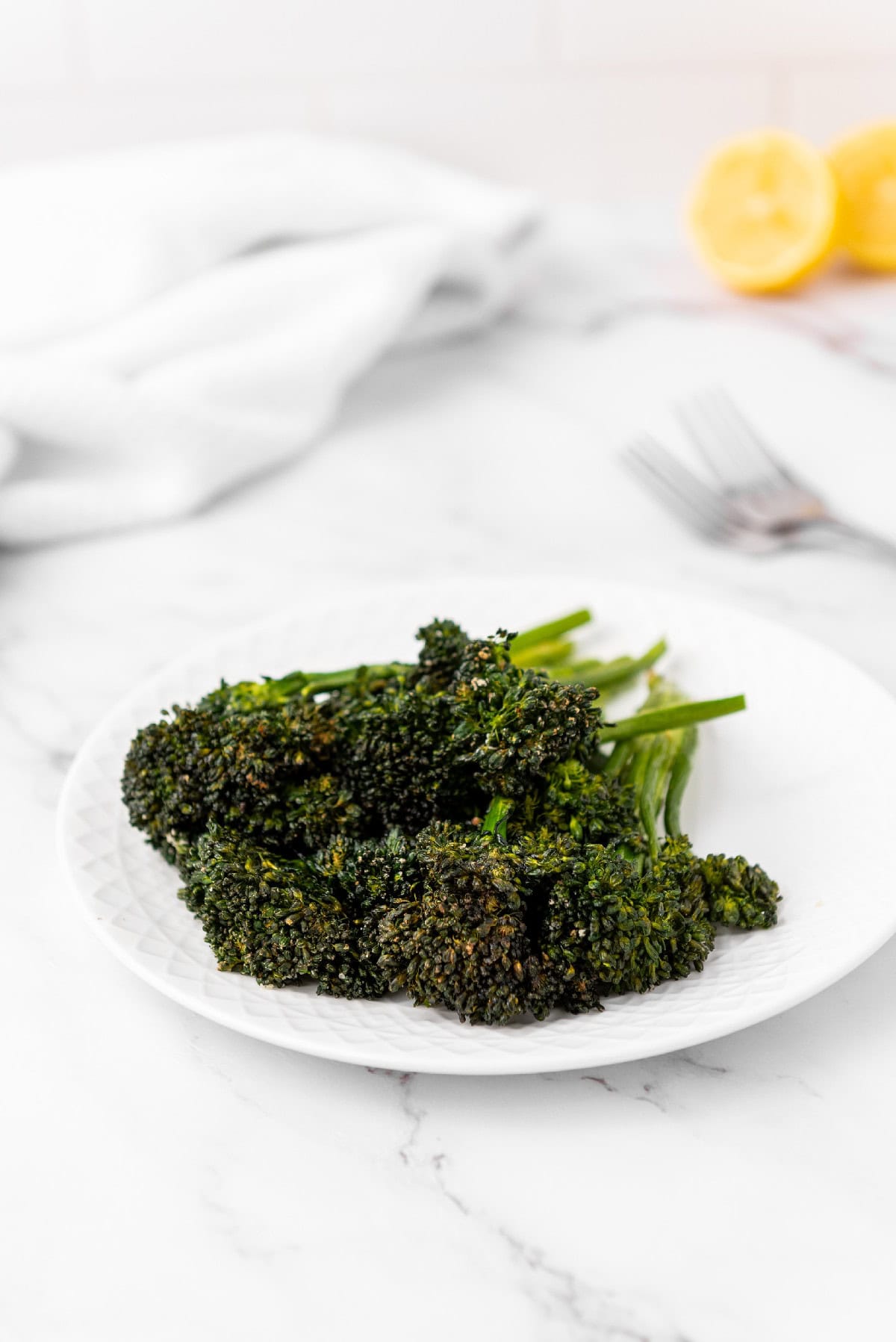 Crispy air fryer broccolini on a white plate, marble surface backdrop.