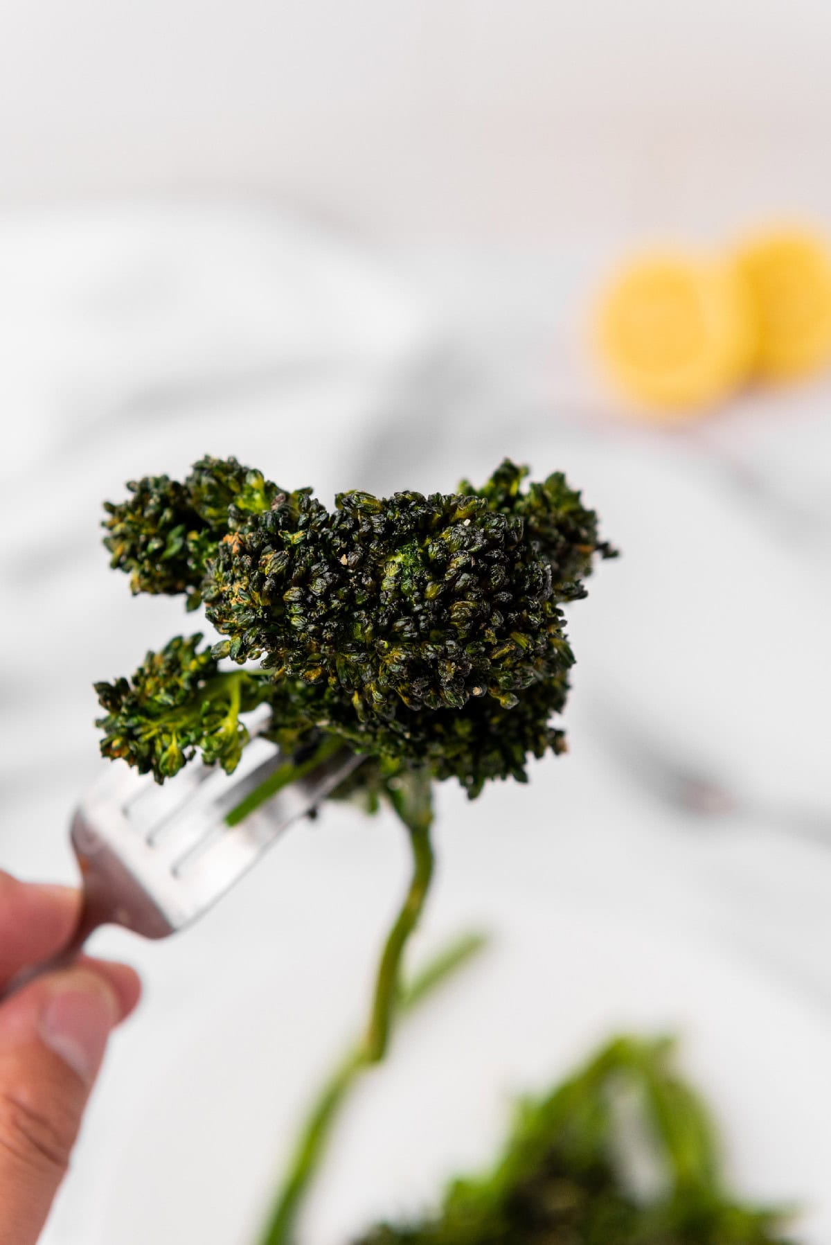 Broccolini floret held up on a fork to show crispy texture.