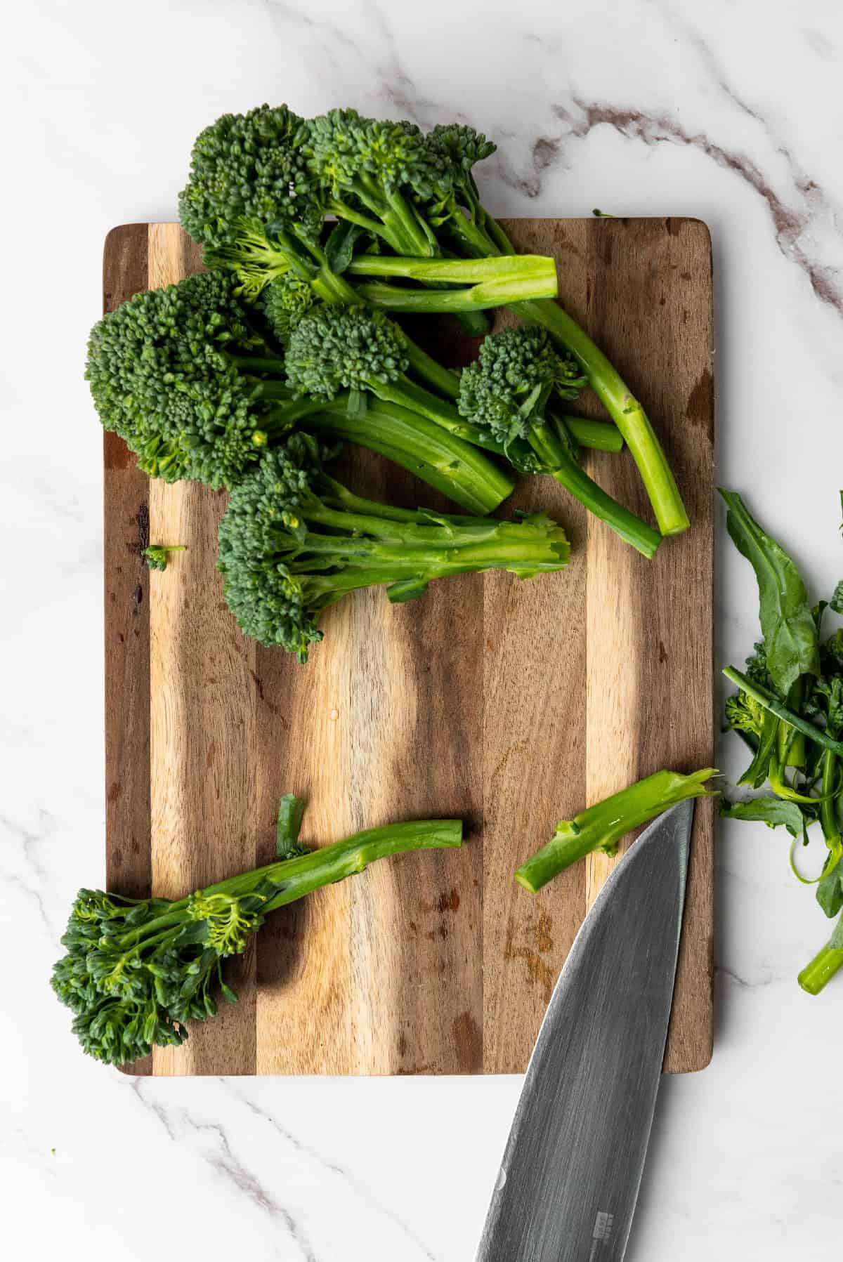Cutting fresh broccolini on a wooden cutting board to trim the ends before cooking.