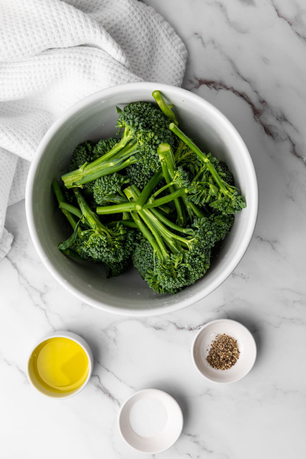 Cutting fresh broccolini on a wooden cutting board to trim the ends before cooking.