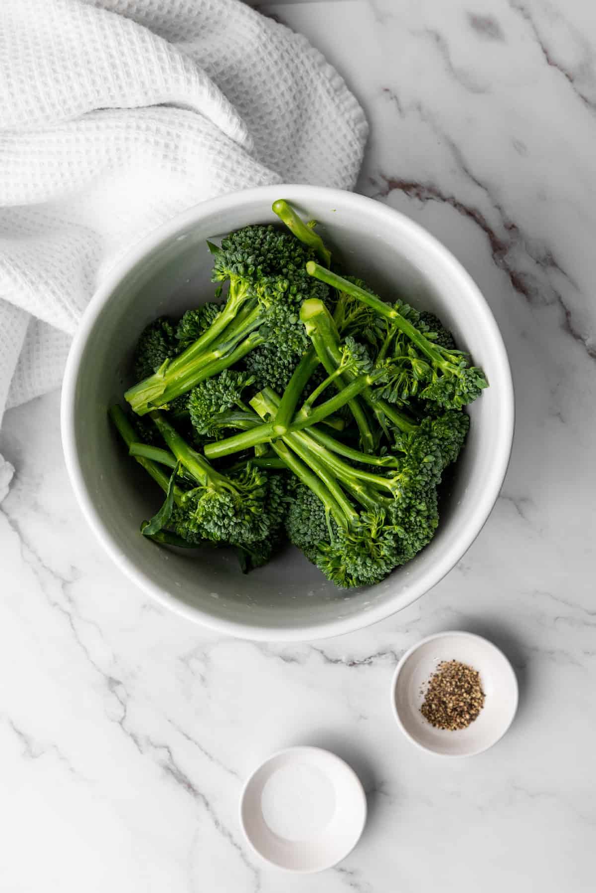 Broccolini in a bowl ready to be seasoned with salt and pepper before air frying.