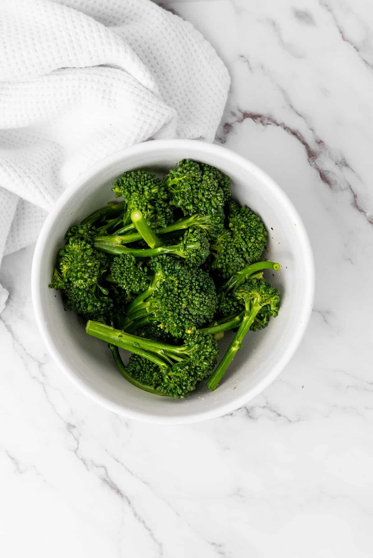 Seasoned broccolini tossed in a bowl with simple olive oil, salt, and pepper.