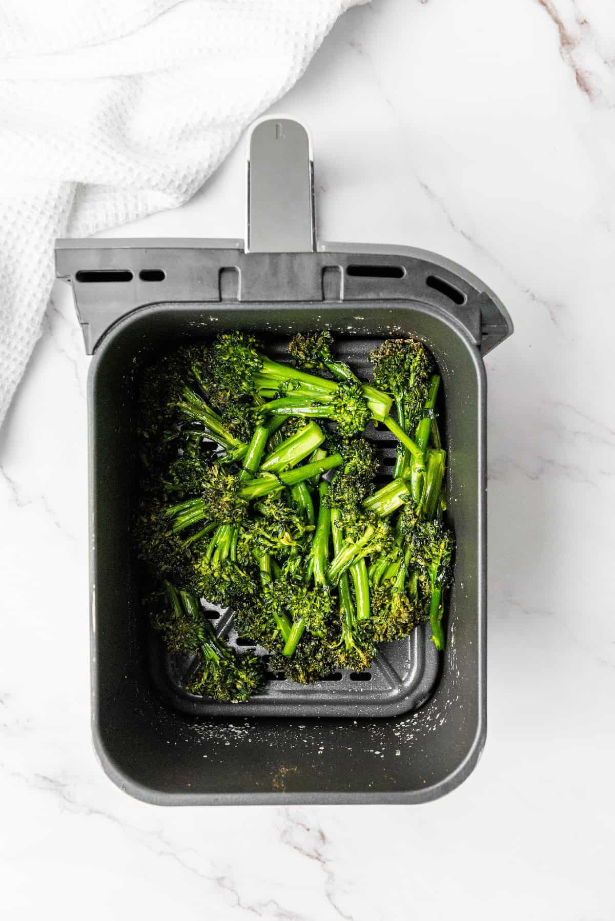 Broccolini arranged inside an air fryer basket, ready to cook until crisp and tender.