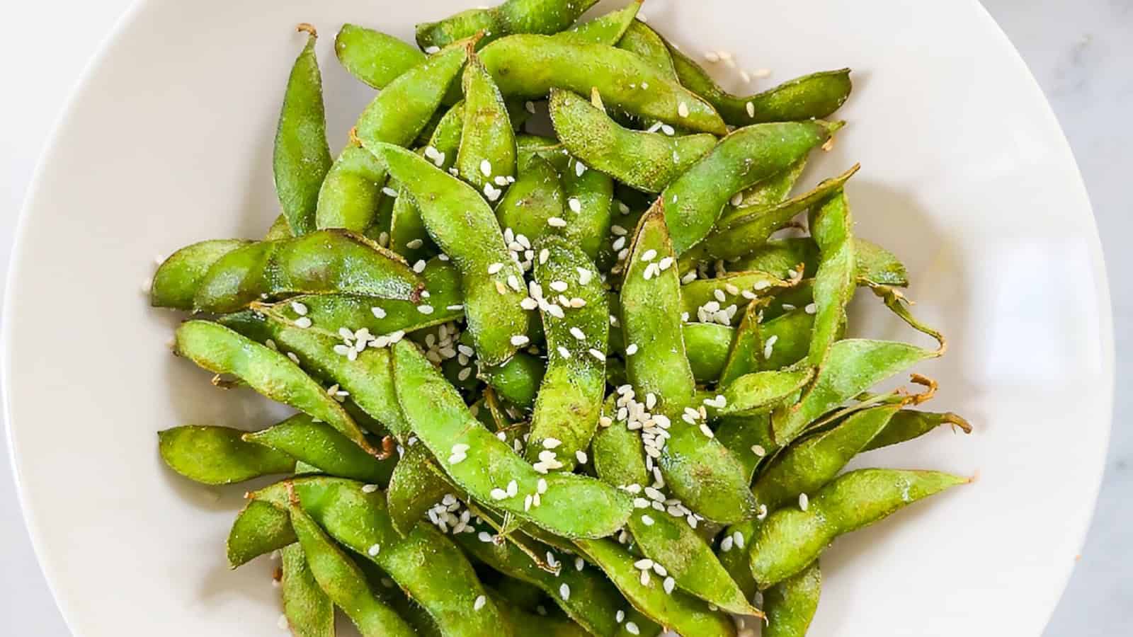 Air fryer edamame served in a white bowl and sprinkled with sesame seeds.