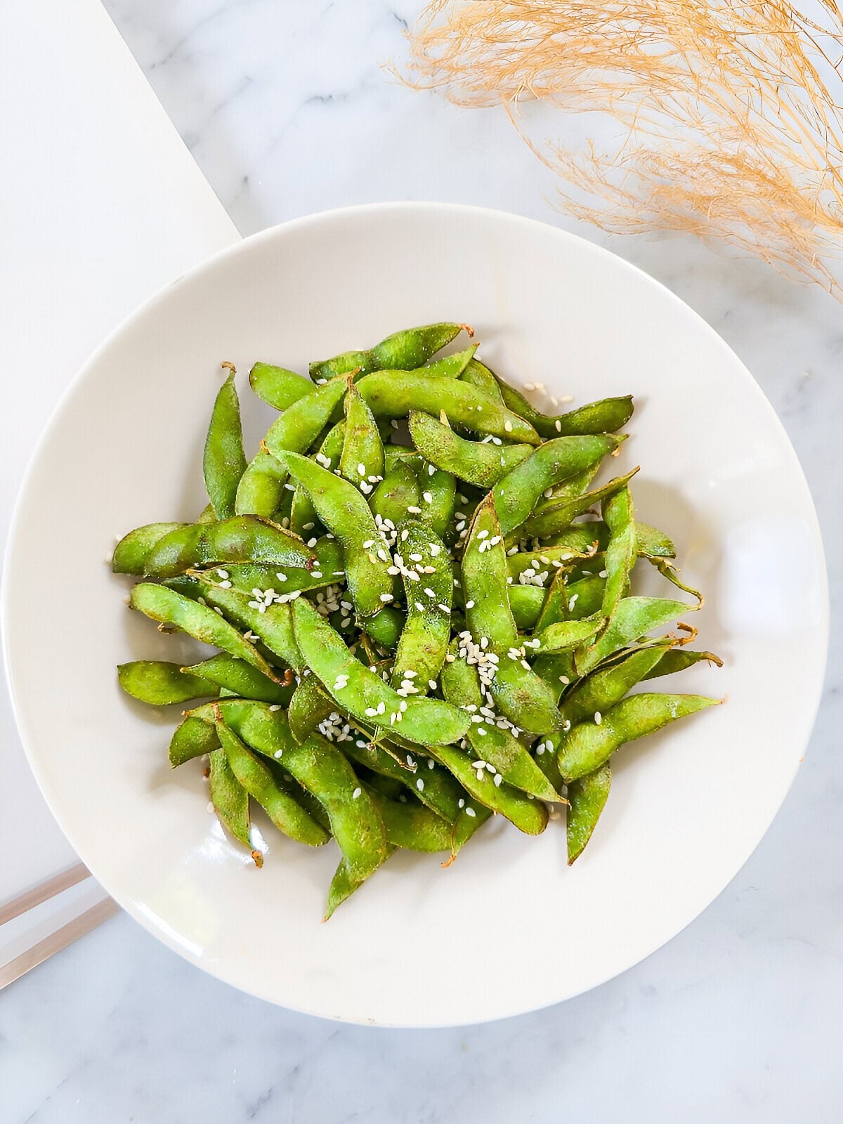 Air fryer edamame served in a white bowl and sprinkled with sesame seeds.
