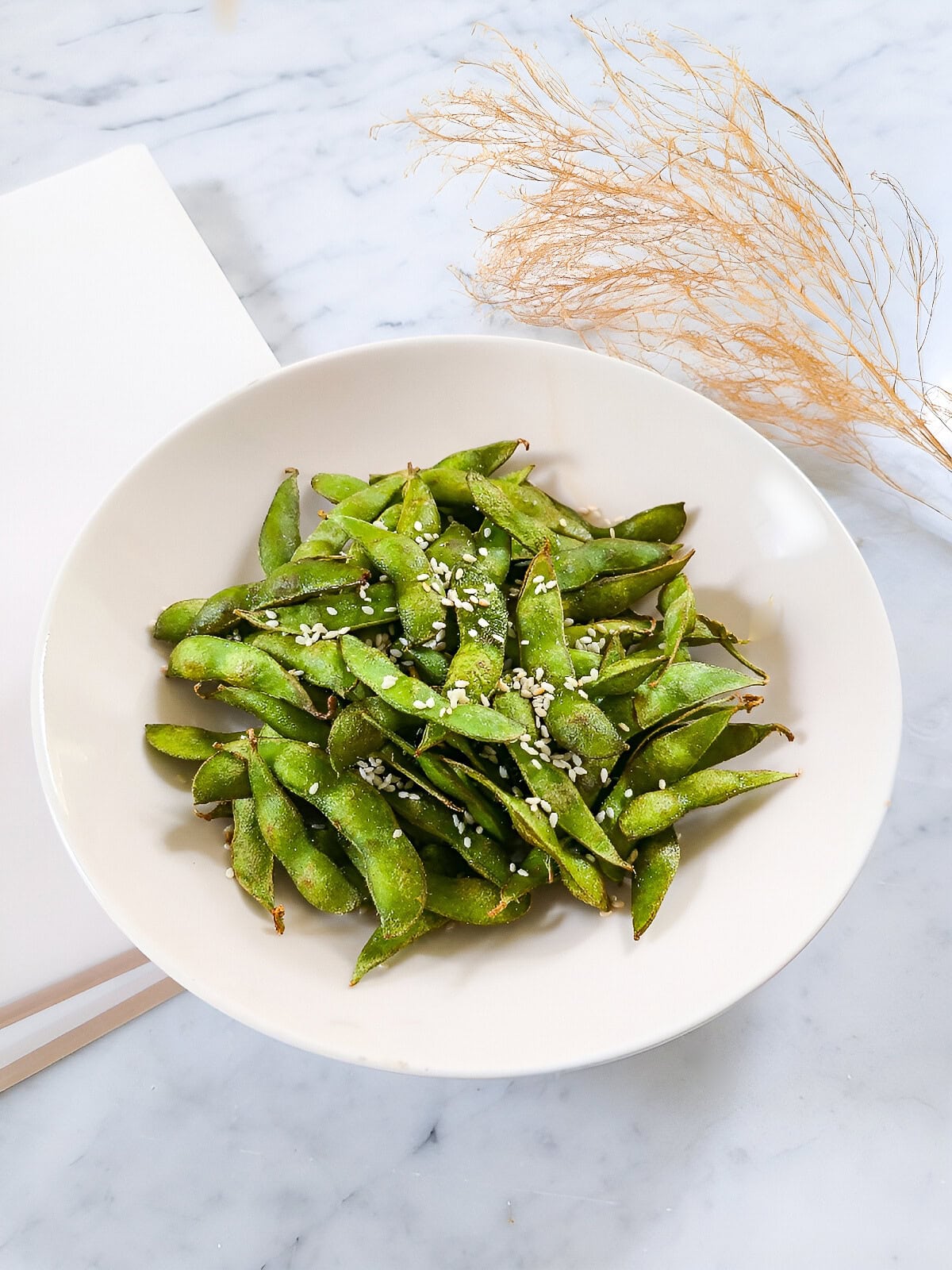 Air fryer edamame plated in a white bowl with chopsticks on a marble background.