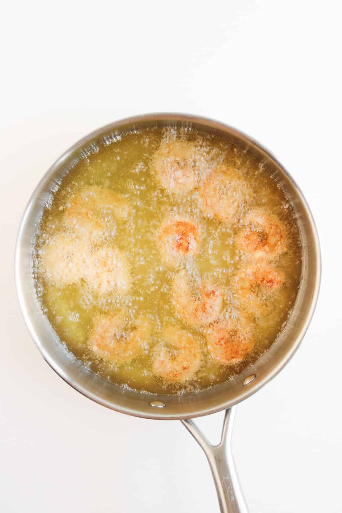 Breaded shrimp frying in hot oil in a skillet.