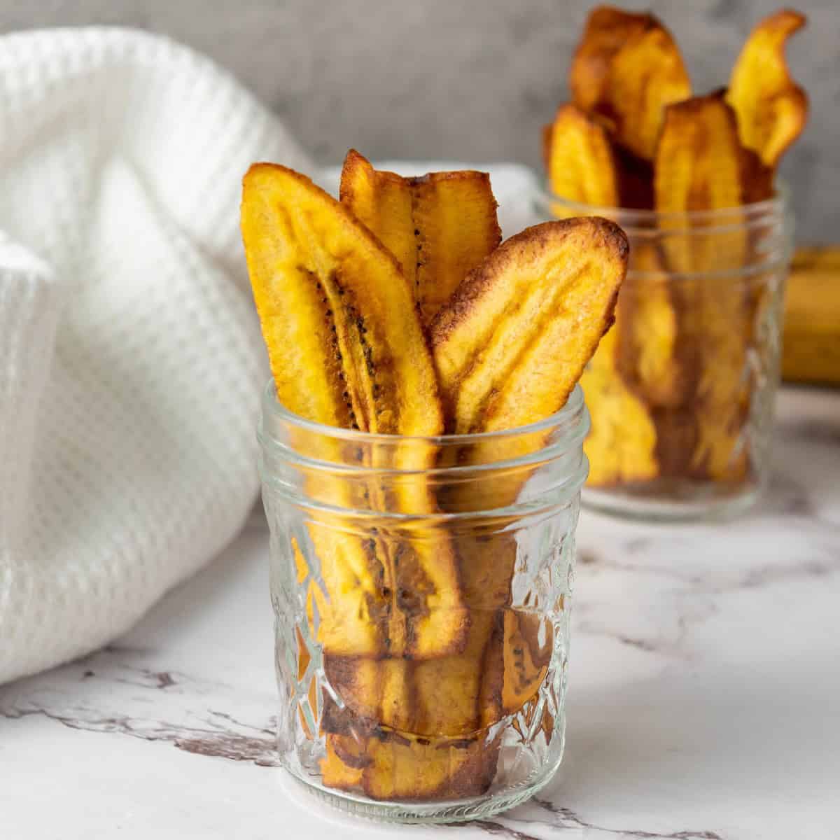 Crispy homemade chifles plantain chips standing upright in a glass jar.