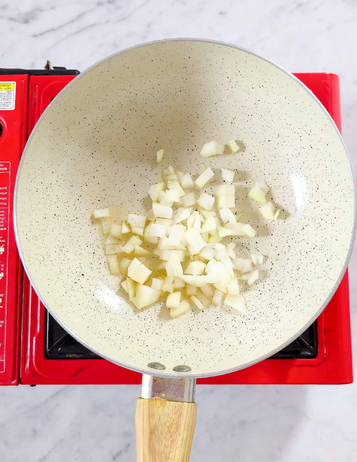 Diced onions sautéing in a pan with oil to start vegetable fried rice.