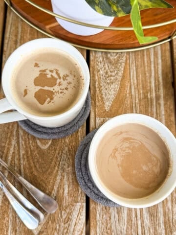 Two mugs of hot cocoa coffee resting on coasters, ready to serve.