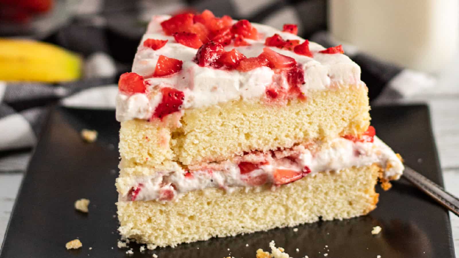 Slice of strawberry banana cake with fluffy vanilla sponge, fresh strawberry pieces, and creamy whipped frosting layered in the middle and on top.