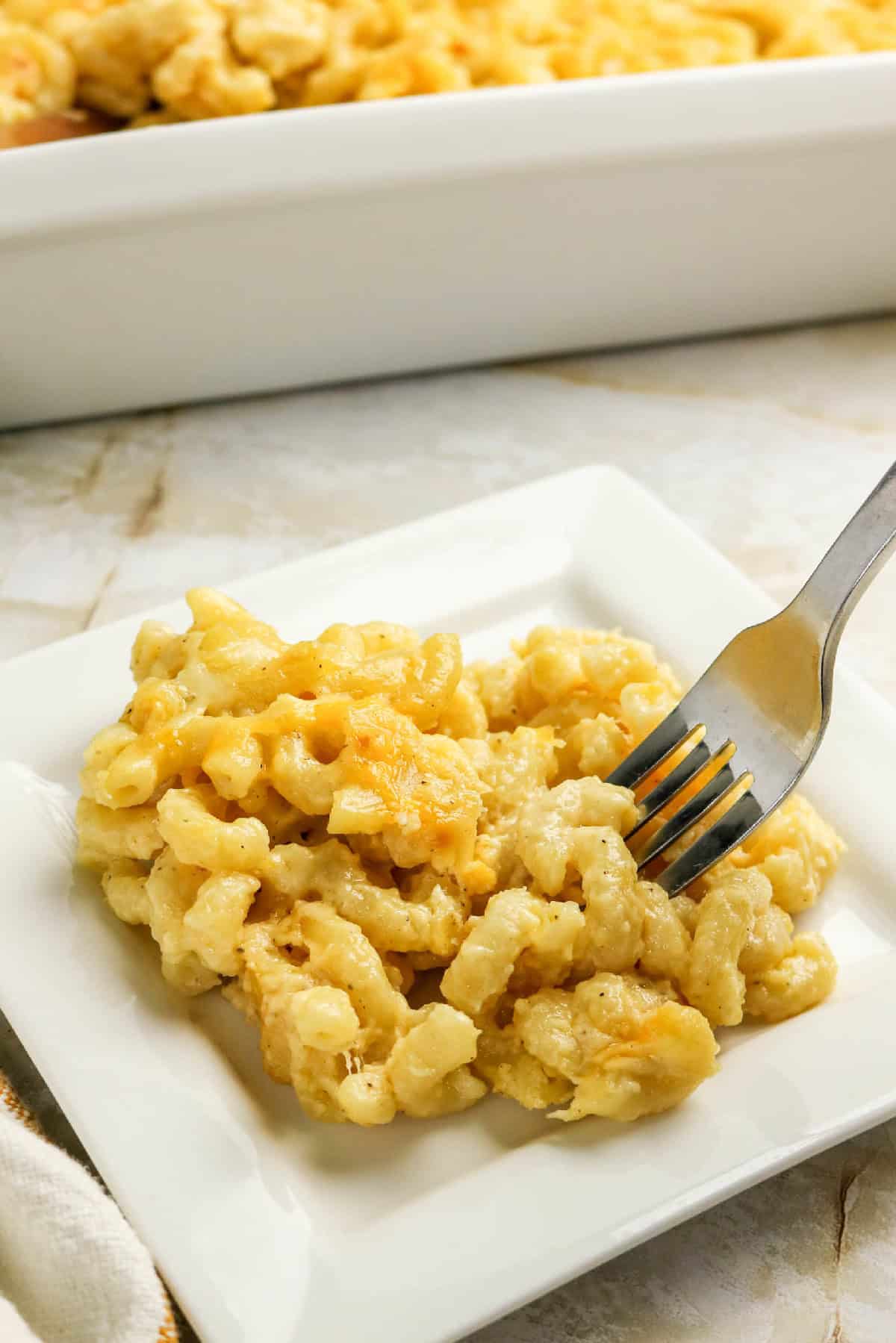 Fork digging into a creamy serving of three-cheese macaroni and cheese on a plate.