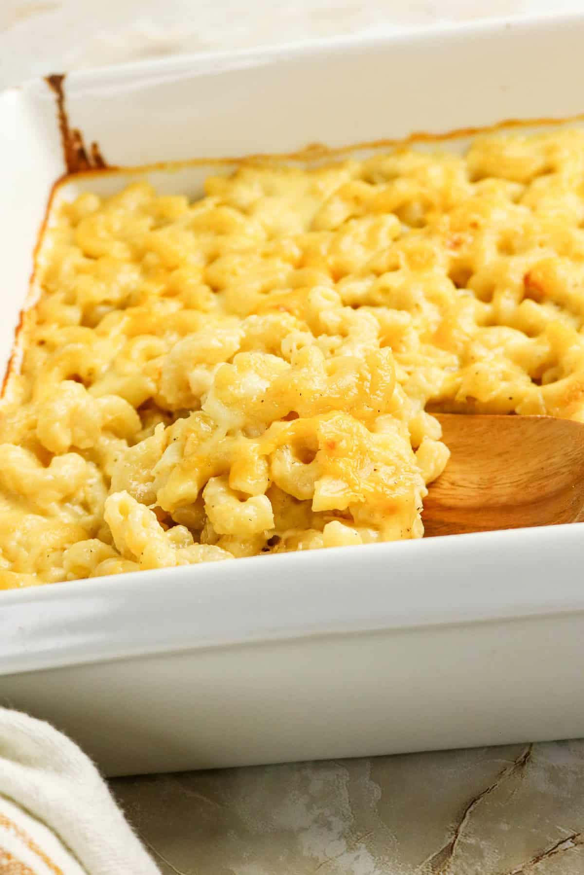 Close-up of creamy baked three-cheese macaroni and cheese being scooped with a wooden spoon.