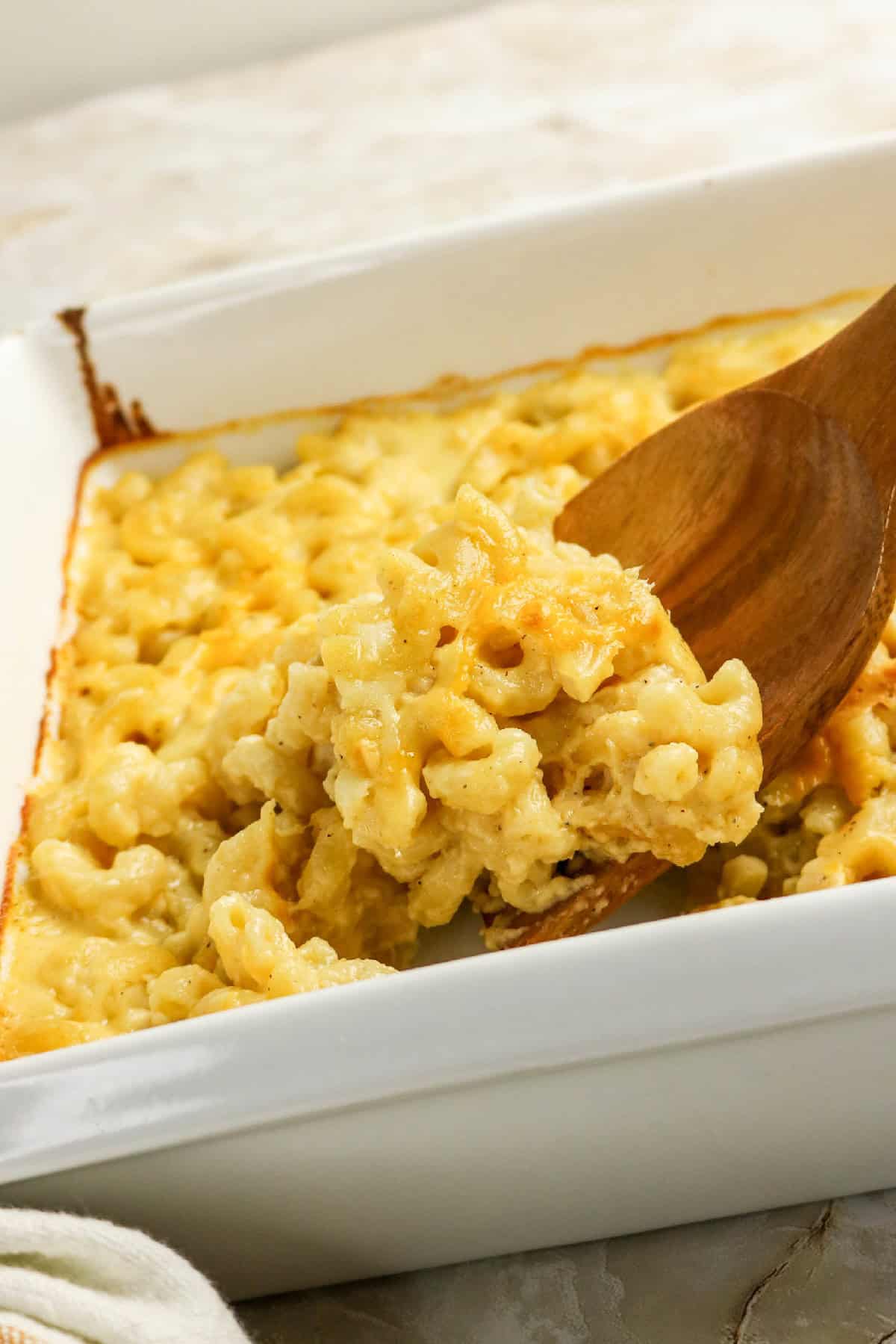 Spoon lifting a serving of gooey three-cheese macaroni and cheese from a baking dish.