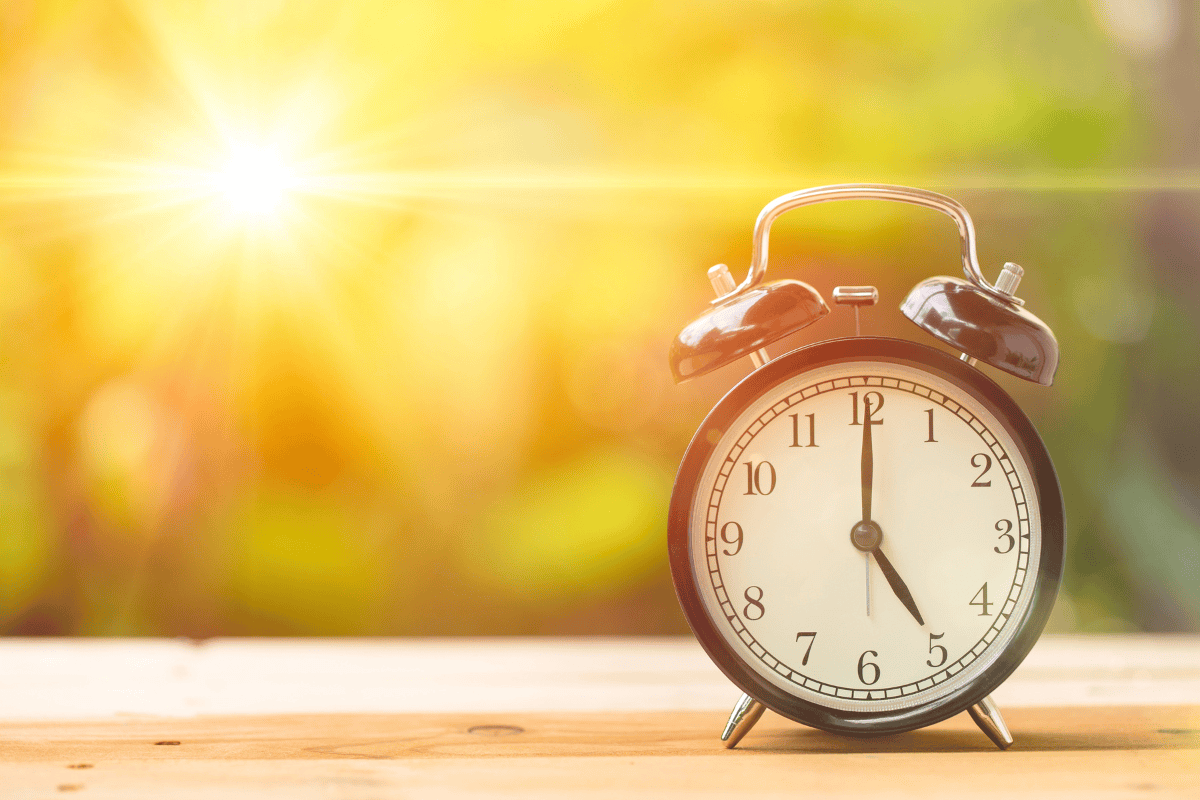 An alarm clock sits on a wooden surface with bright sunlight in the background.