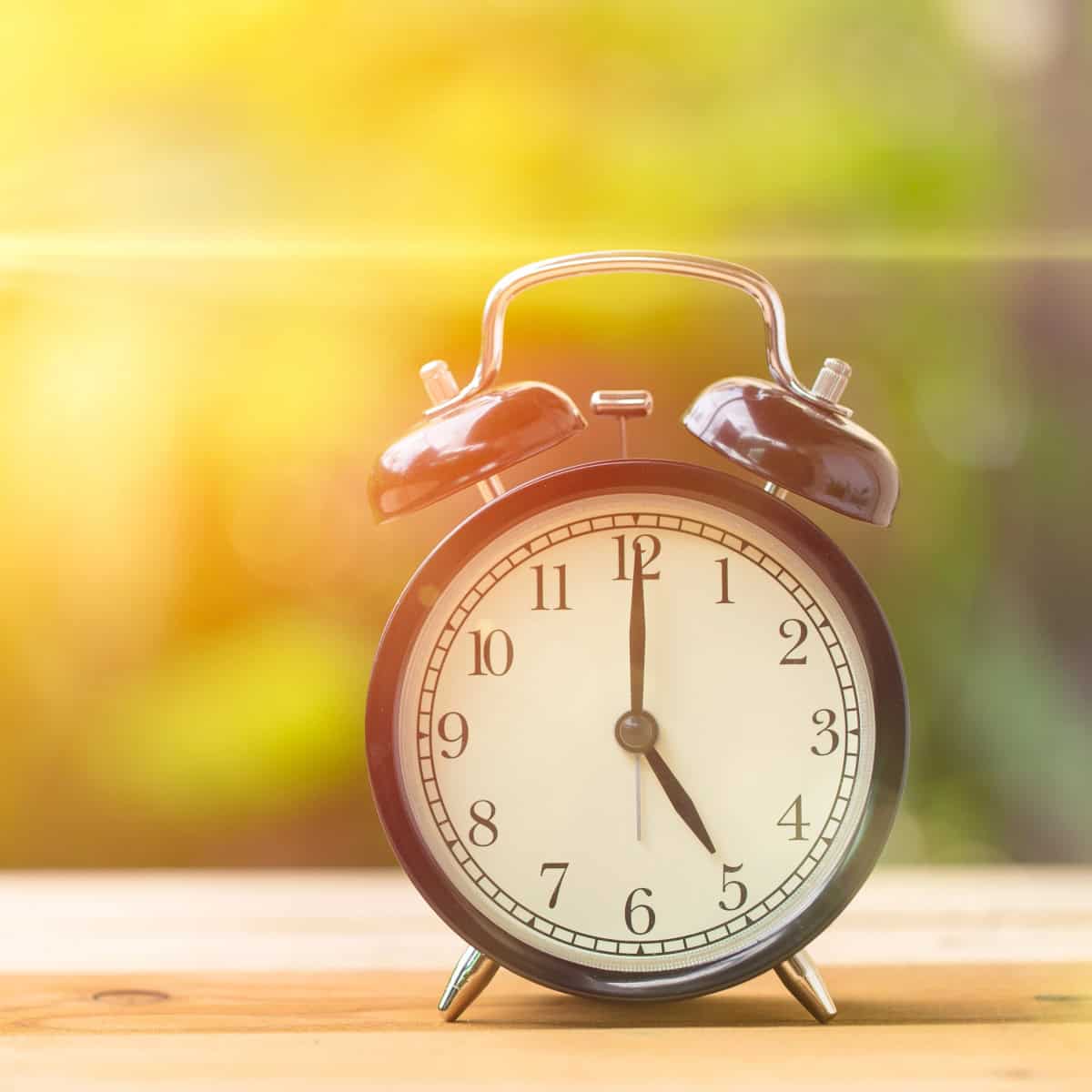 An alarm clock rests on a wooden surface, illuminated by bright sunlight in the background.