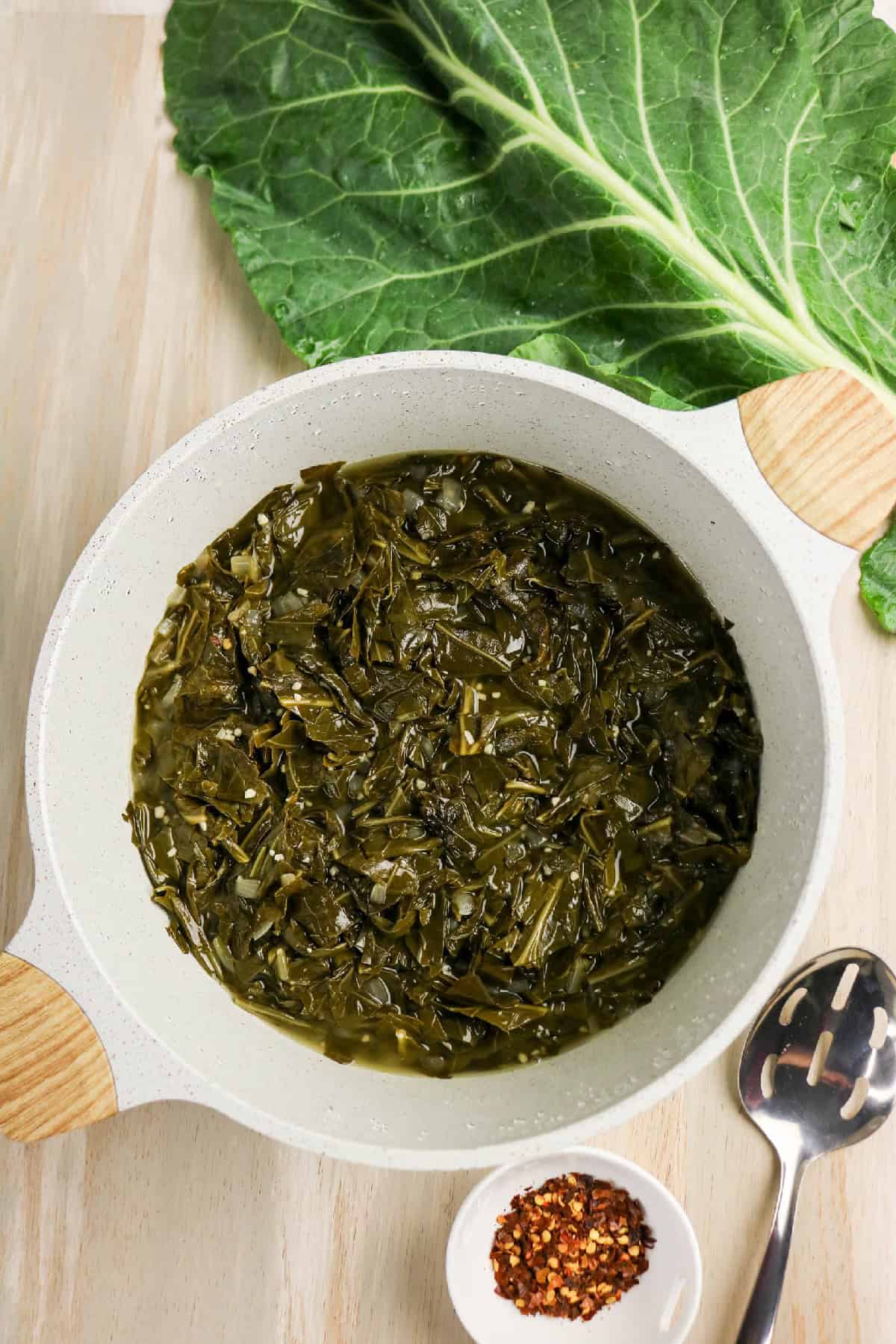Braised collard greens simmered in a light broth in a white pot.