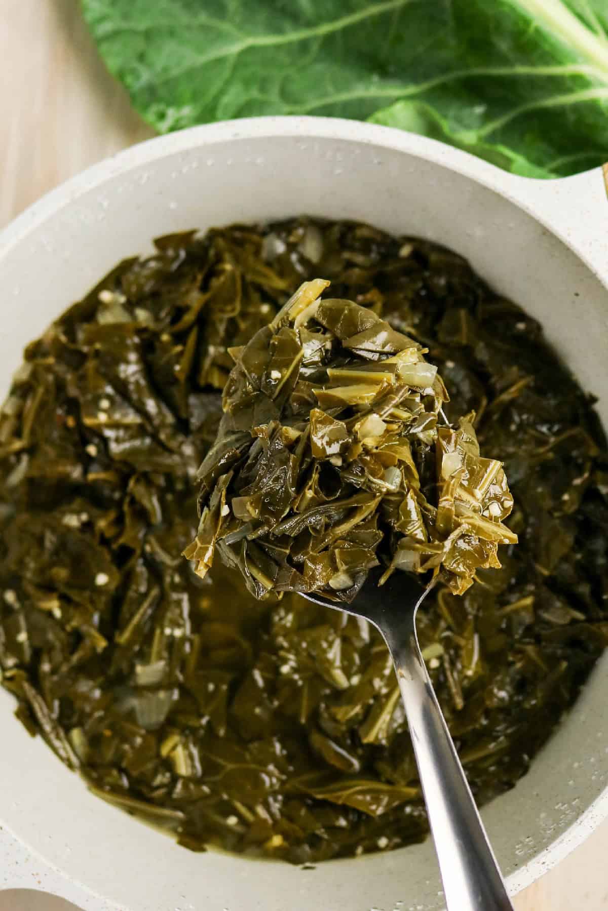 Spoonful of tender braised collard greens lifted from the pot.