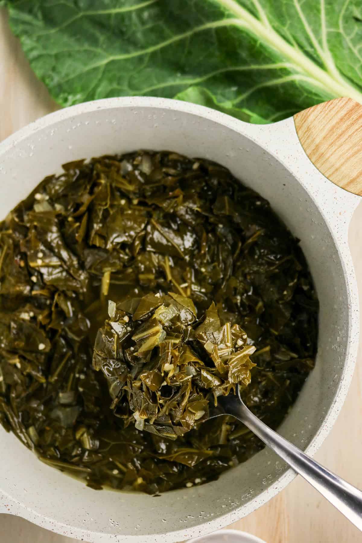 Spoon lifting glossy braised collard greens from the pot.